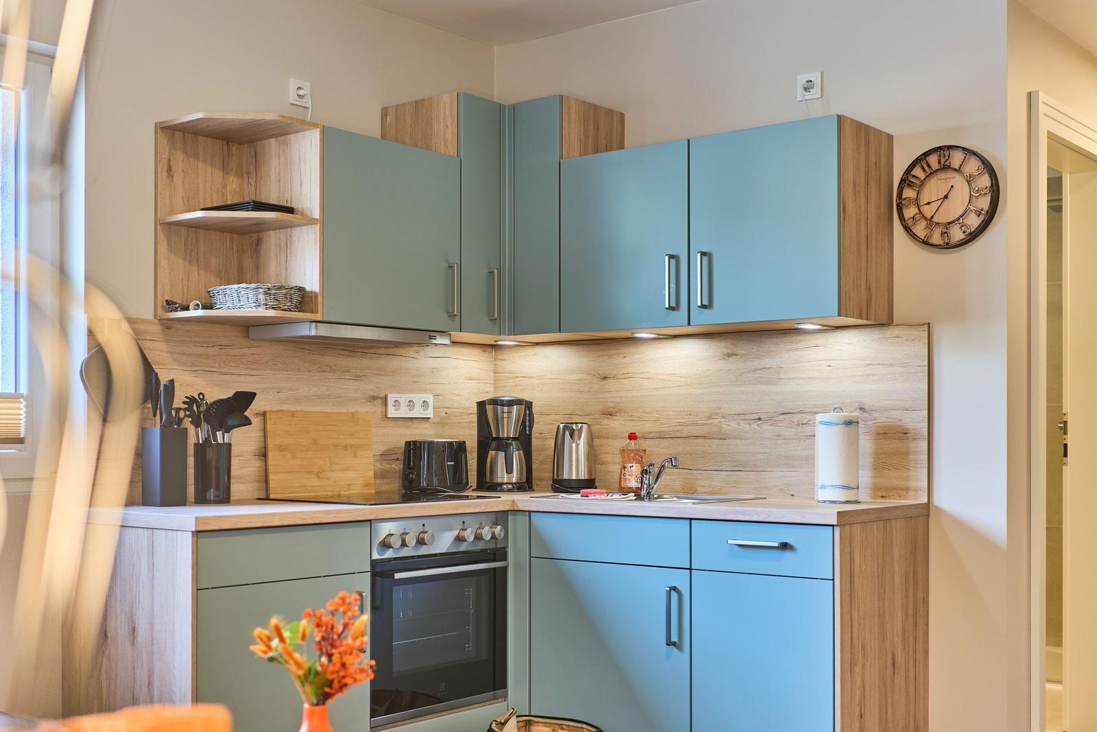 Küche mit blauen Schränken und Holzoptik, Spüle, Herd und Küchenutensilien.