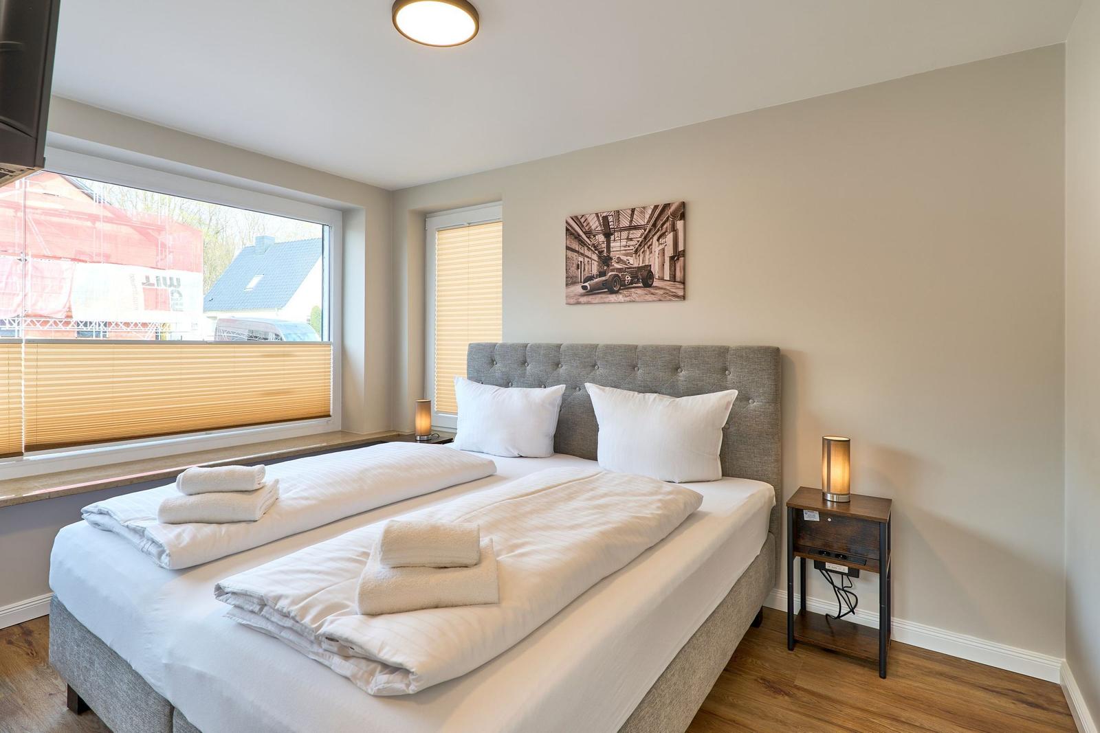 Schlafzimmer mit Bett, Nachttisch und Fenster. Auf dem Bett liegen Handtücher.