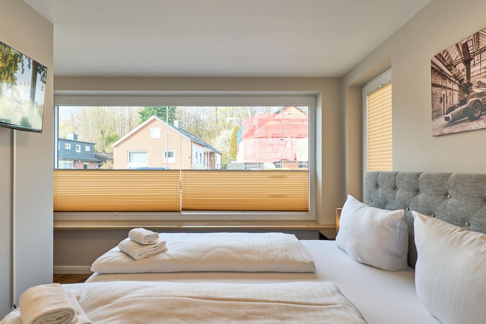 Schlafzimmer mit Bett, Fenster und Wandbild. Auf dem Bett liegen Handtücher.