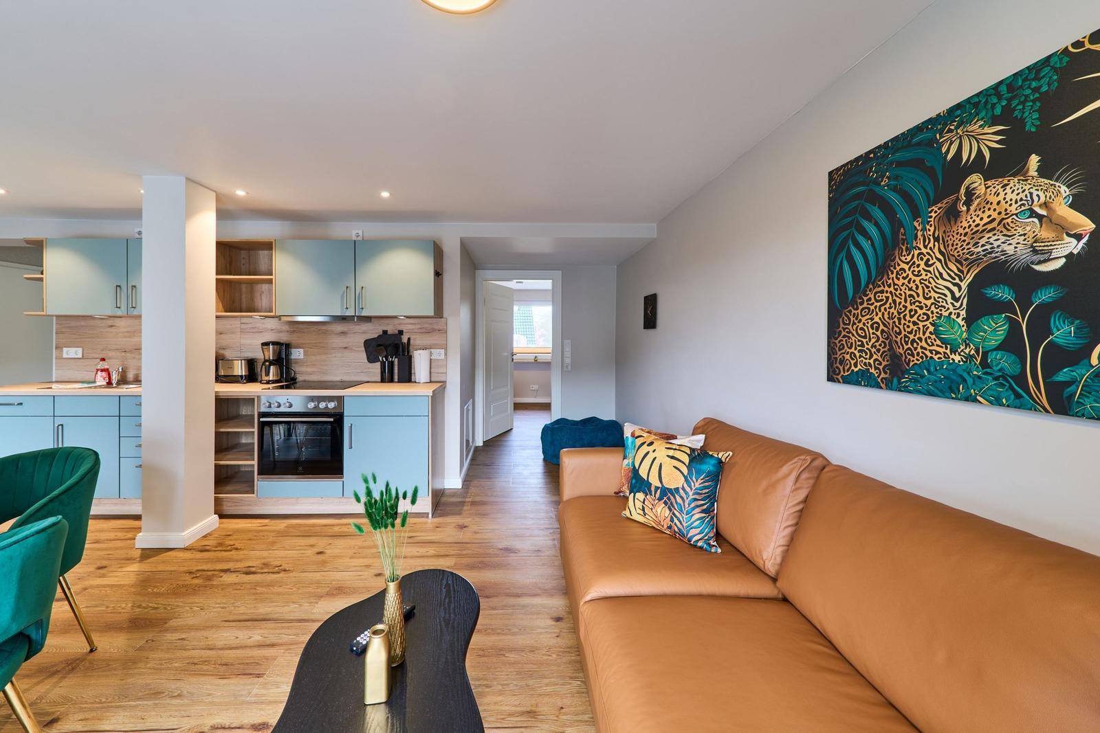 Wohnbereich mit braunem Sofa, Küchenbereich und Wandbild eines Leoparden.