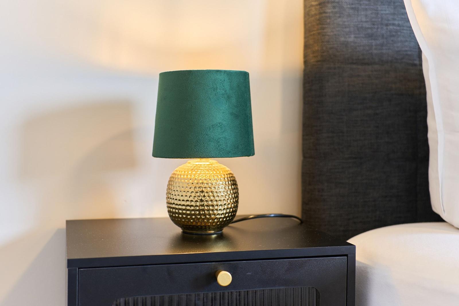 Tischlampe mit grünem Schirm auf Nachttisch neben Bett
