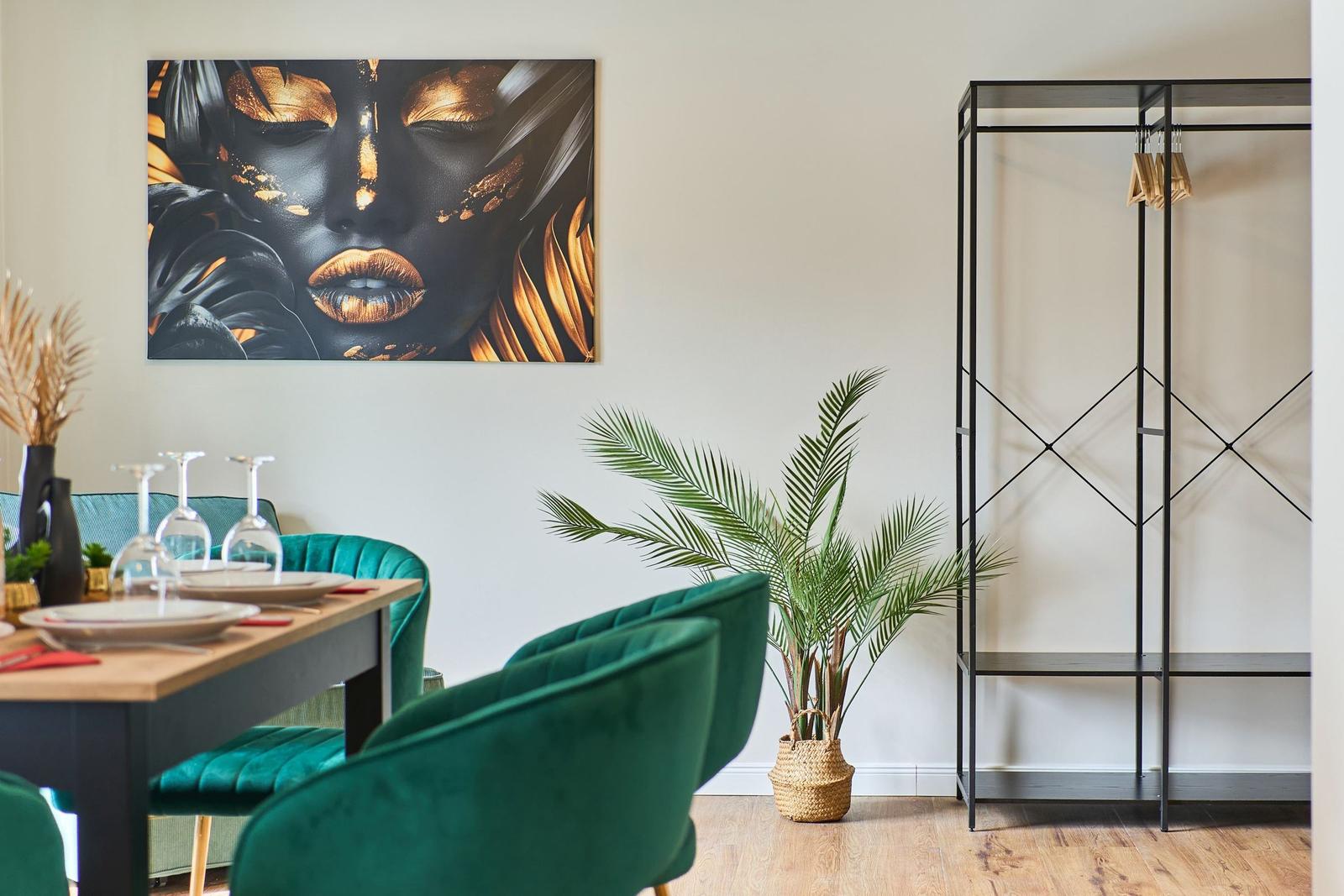 Esszimmer mit grünen Stühlen, Wandbild und Pflanze. Kleiderständer an der Wand.