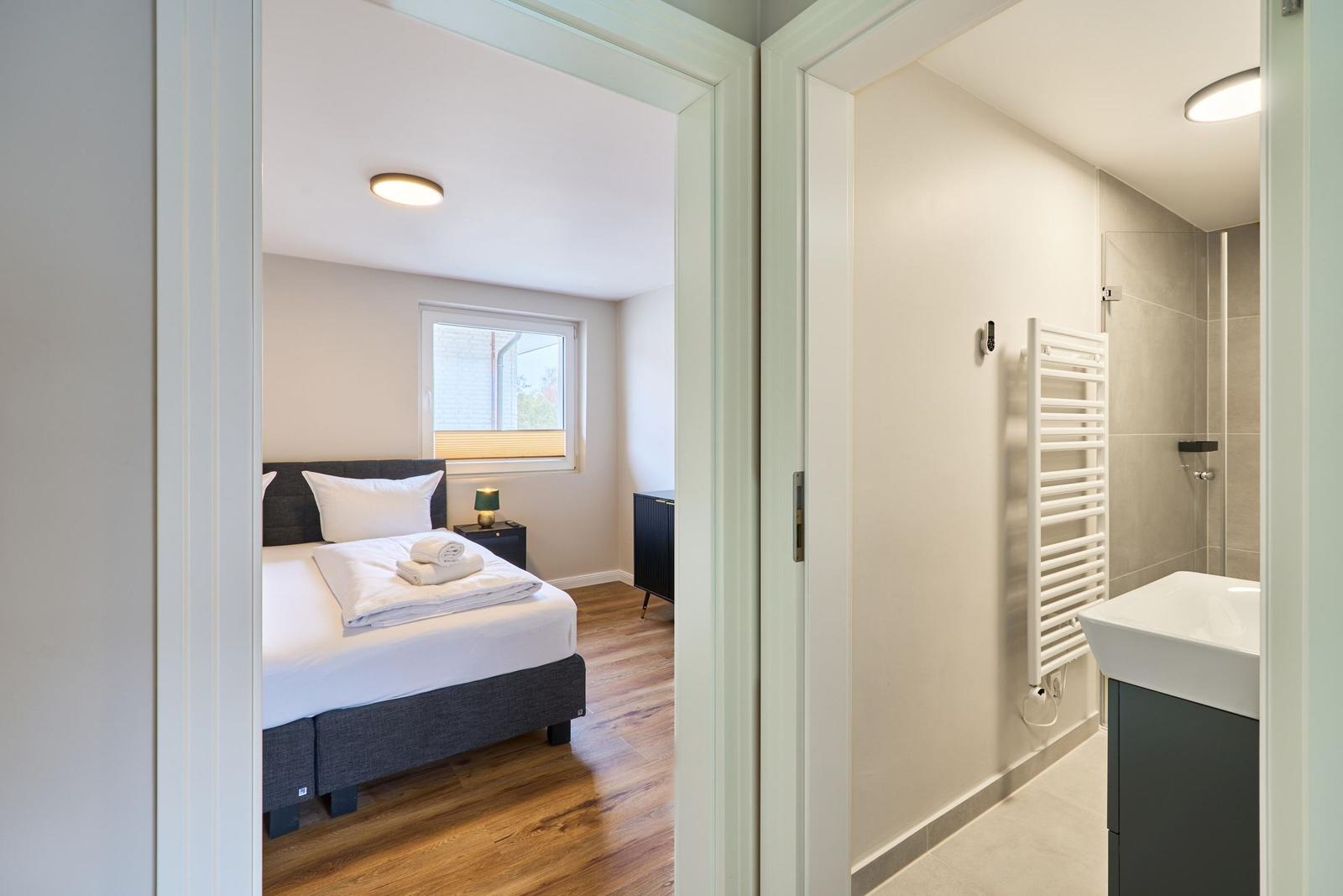 Schlafzimmer mit Bett und Fenster. Nebenraum mit Waschbecken und Heizung.