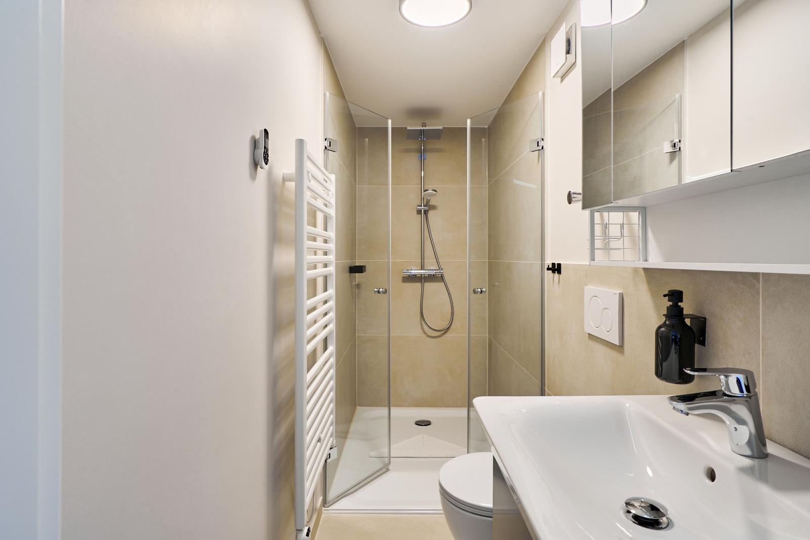 Badezimmer mit Dusche, Waschbecken und Toilette. Weiße Fliesen und Spiegelschrank.