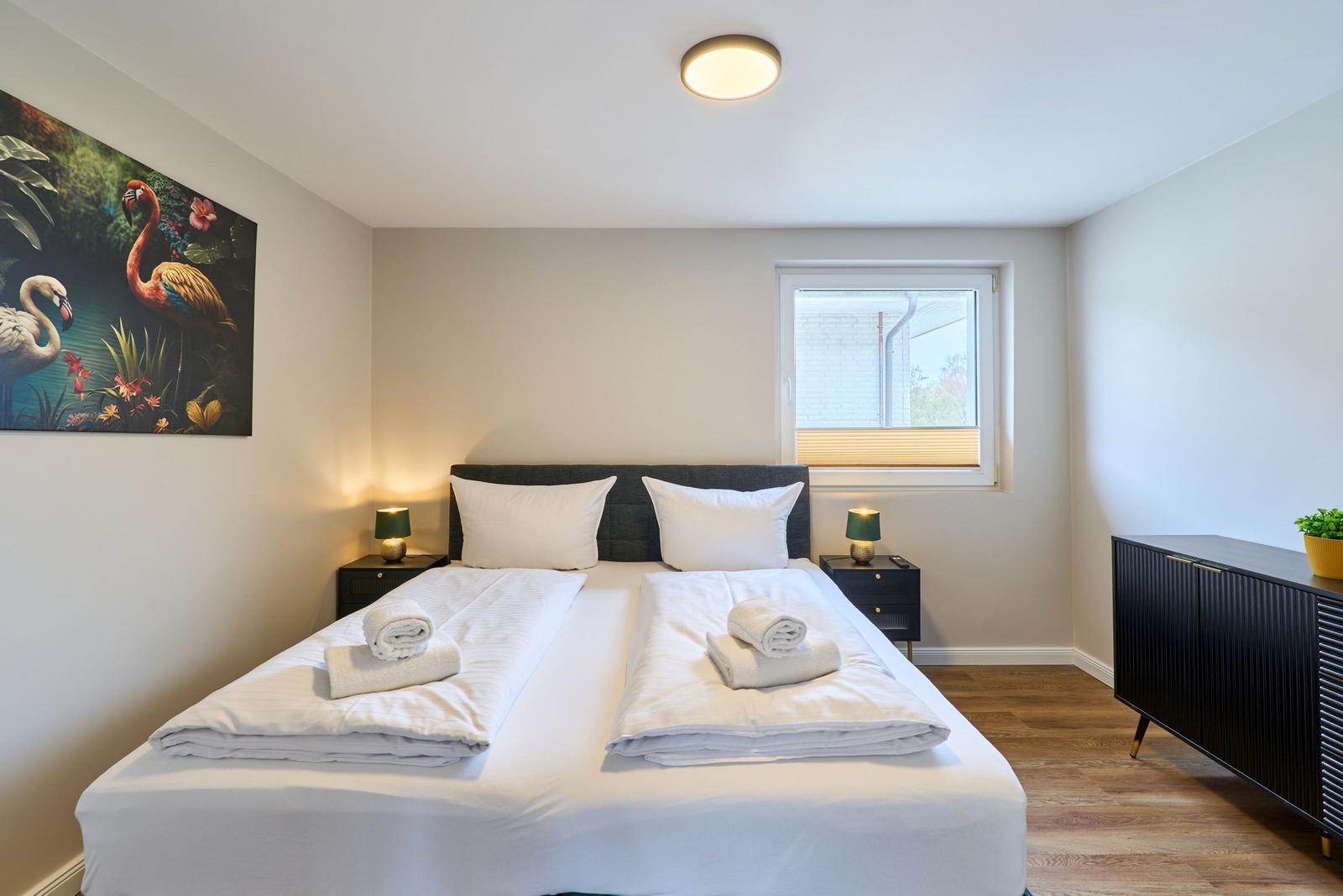 Schlafzimmer mit Doppelbett, zwei Nachttischen und Wandbild mit Flamingos.