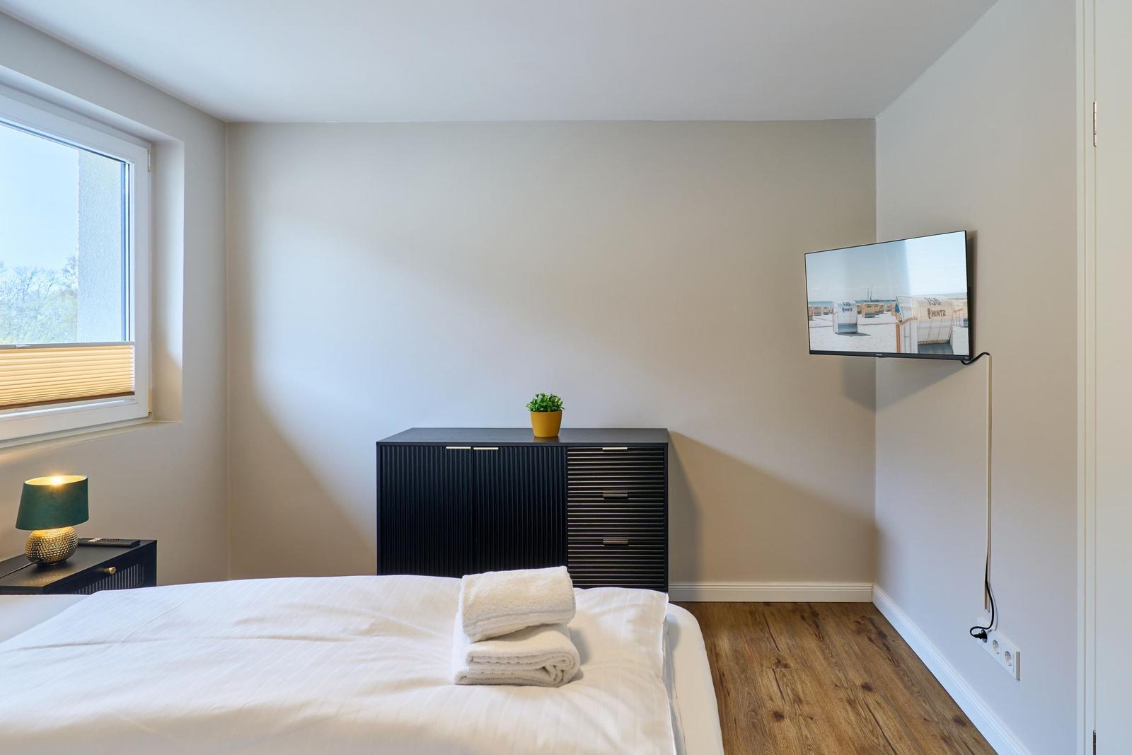 Schlafzimmer mit Bett, Schrank, Fernseher und Fenster.