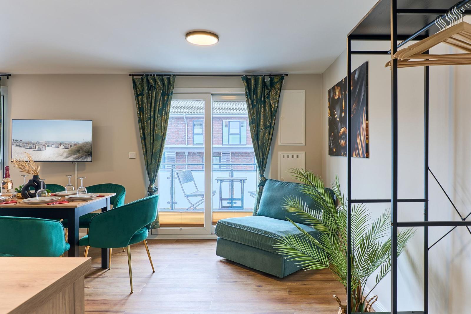 Wohn- und Essbereich mit grünem Sofa, Tisch und Stühlen, Balkon und Wandbild.
