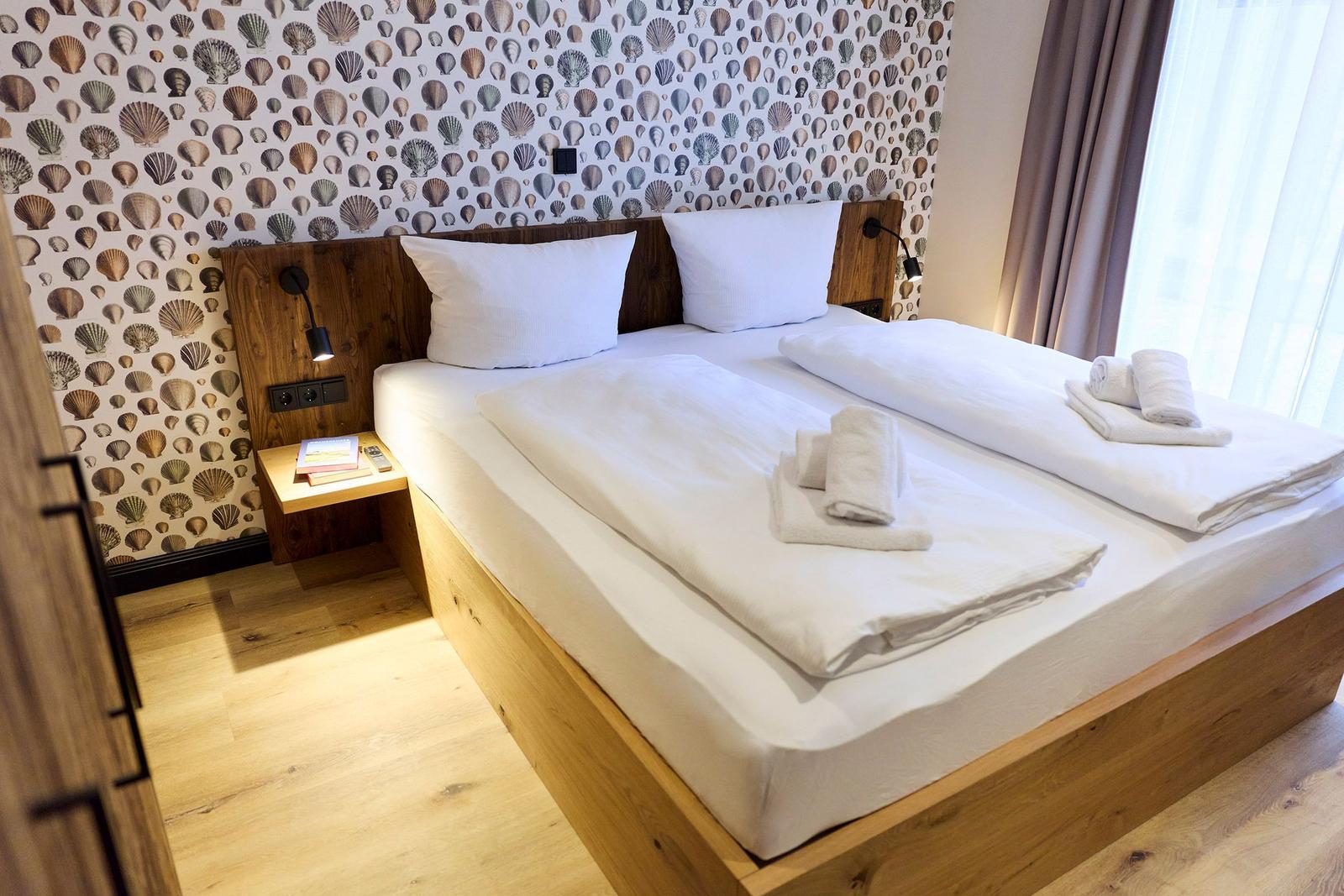 Ein Bett mit weißer Bettwäsche, einem Holzkopfteil und einer Muschelwandtapete.