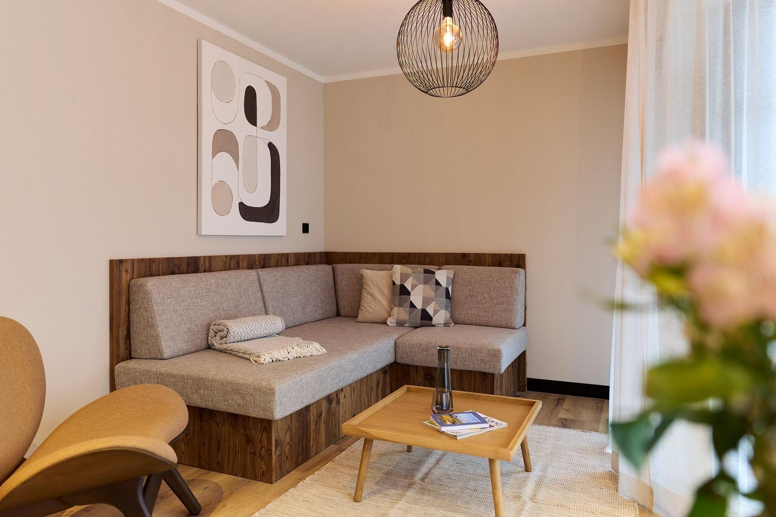 Ein Wohnbereich mit Ecksofa, Holztisch und moderner Deckenleuchte.