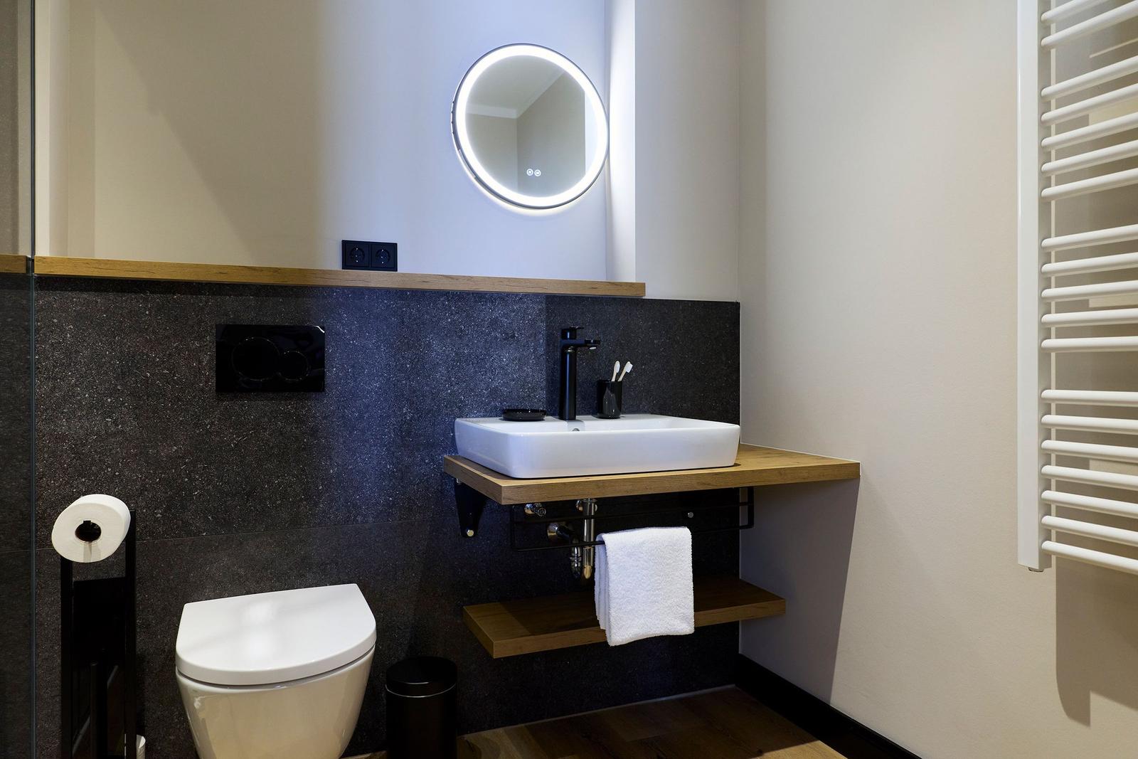 Badezimmer mit Waschbecken, Toilette und runden Spiegel.
