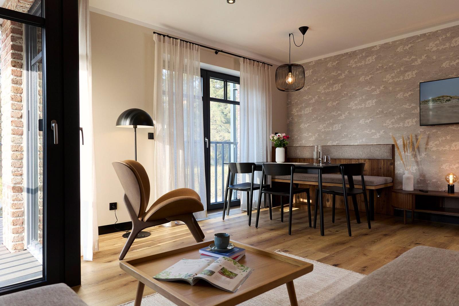 Ein Essbereich mit Tisch, Stühlen und einer Bank an der Wand. Vor dem Fenster steht ein Sessel.