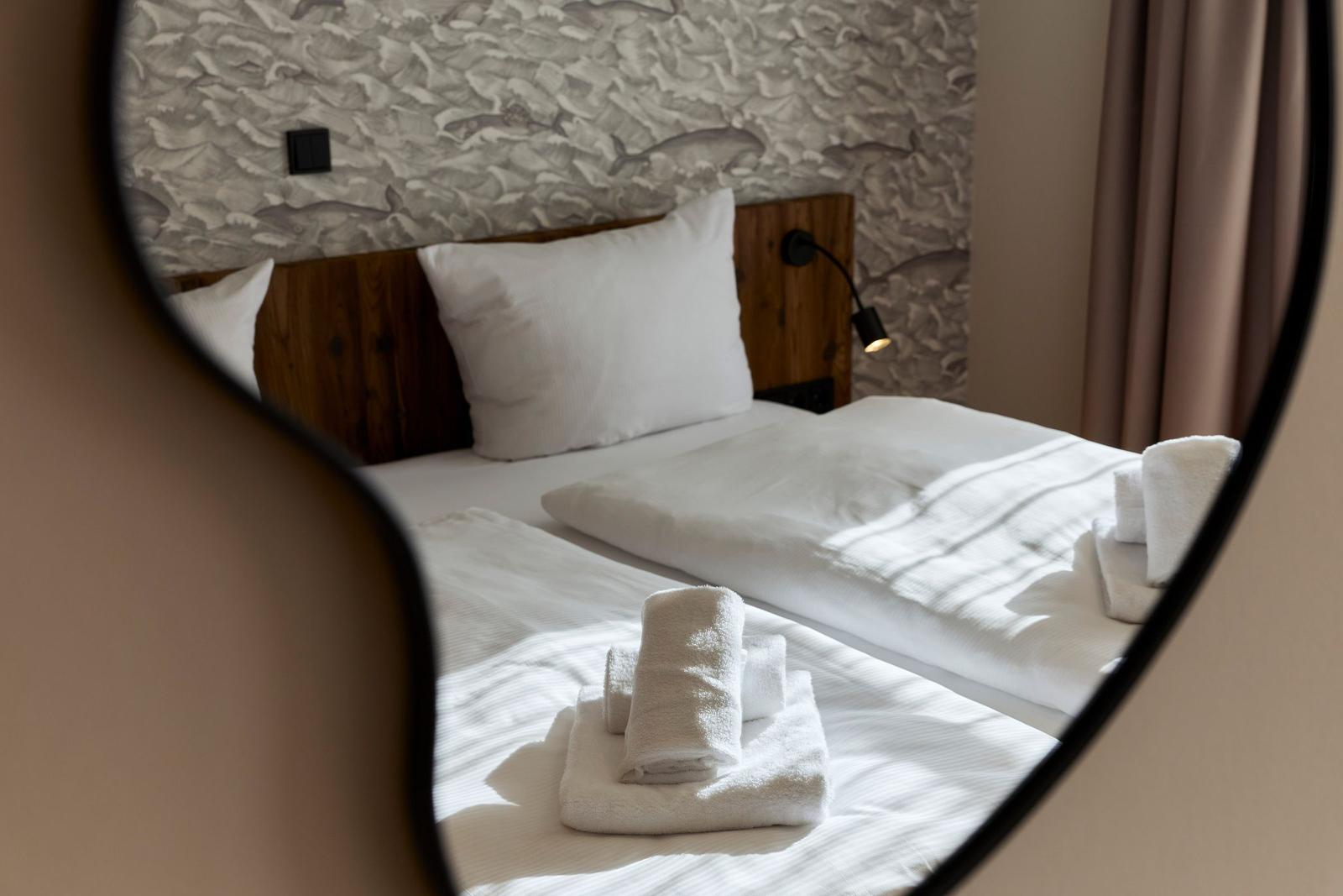 Doppelbett mit weißen Laken und gefalteten Handtüchern im Spiegel