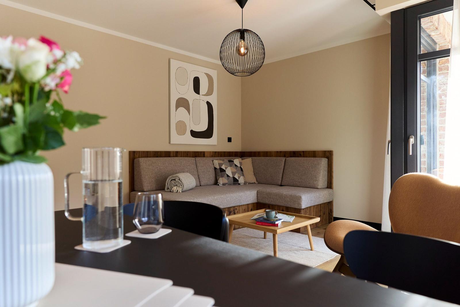 Wohnbereich mit Sofa, Tisch und Wandbild. Fenster mit Blick auf Backsteinmauer.
