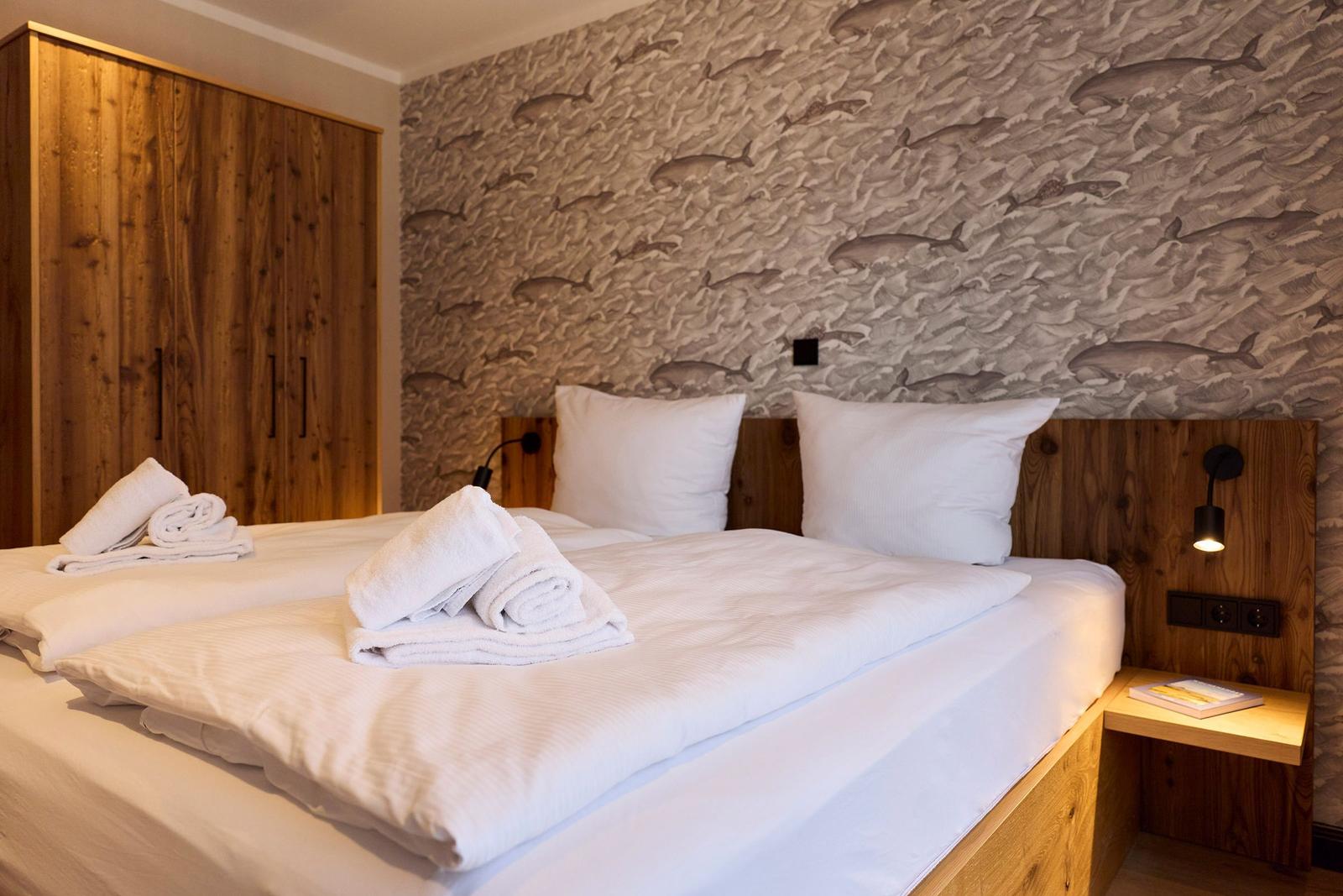 Doppelbett mit weißen Bettwäsche, Holzgestell und Fischmotiv-Wandtapete.