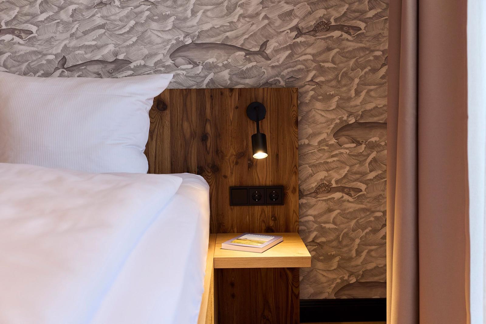 Schlafzimmer mit Holz-Kopfteil, Wand mit Meerestier-Motiv und Nachttisch mit Buch.