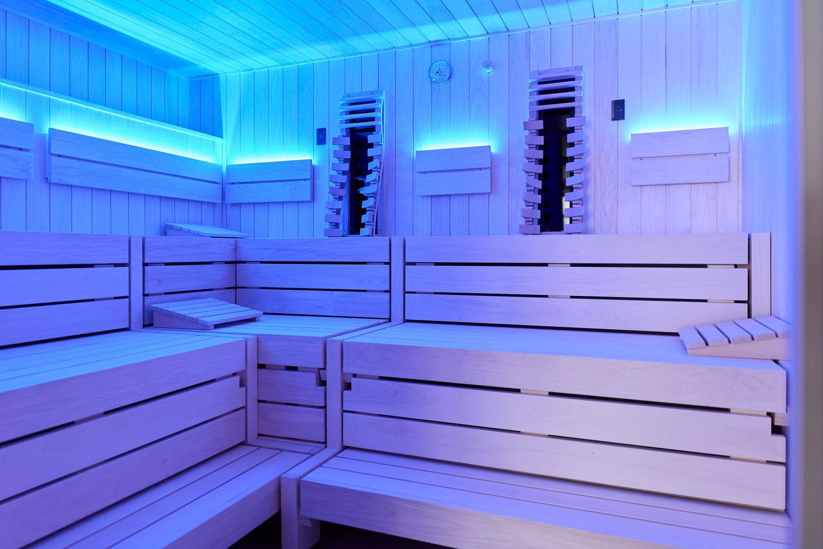 Sauna mit Holzbank und blauer Beleuchtung an den Wänden.