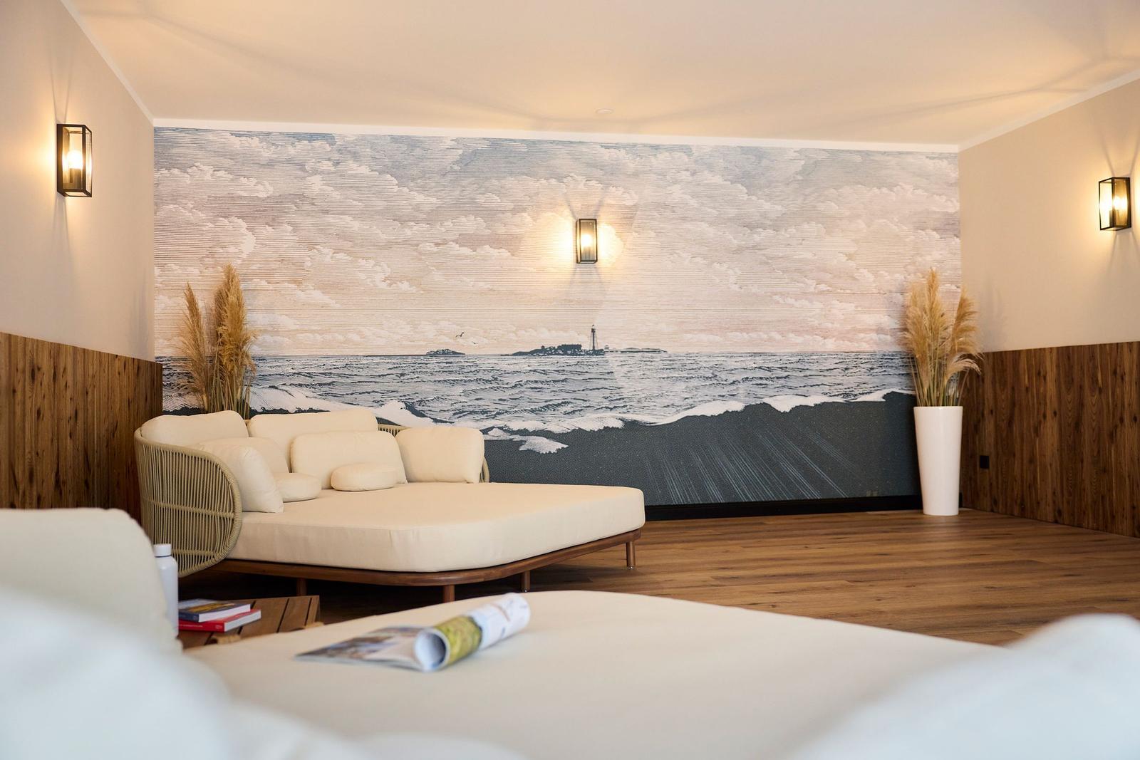 Ein Raum mit einem großen Wandbild eines Meeres und einer Laterne. Ein Sofa und ein Bett sind sichtbar.