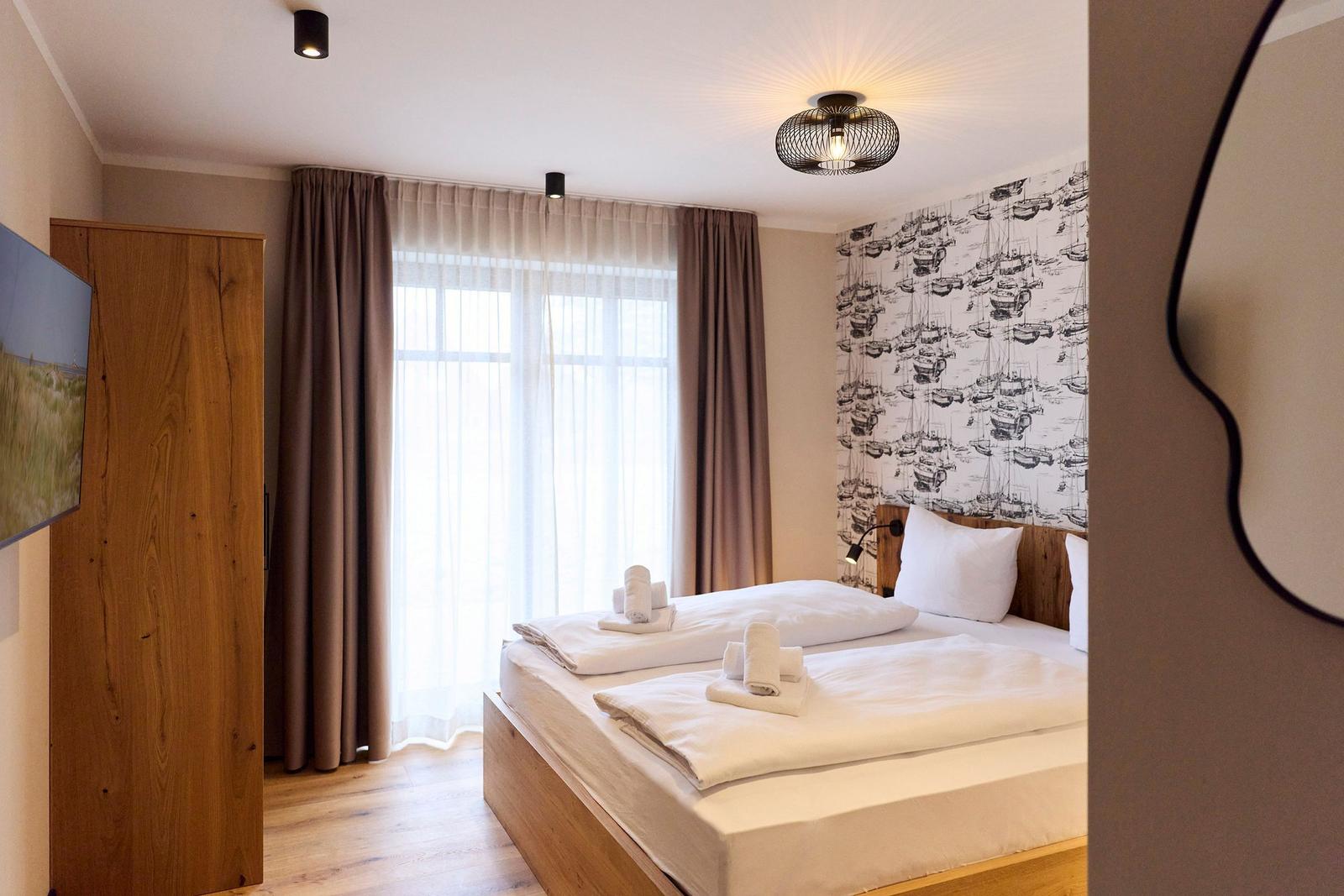 Schlafzimmer mit Bett, Gardinen und Wandtapete mit Schiffsmotiv.