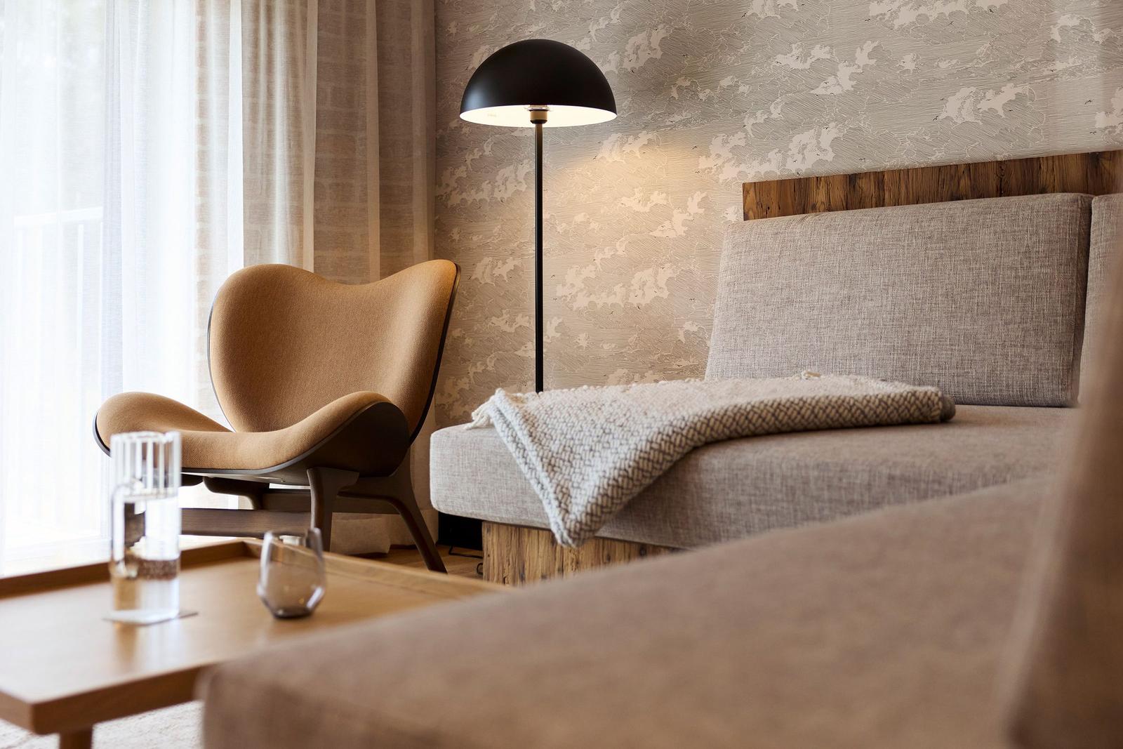Ein Raum mit einem Sessel, einem Bett und einer Stehlampe.