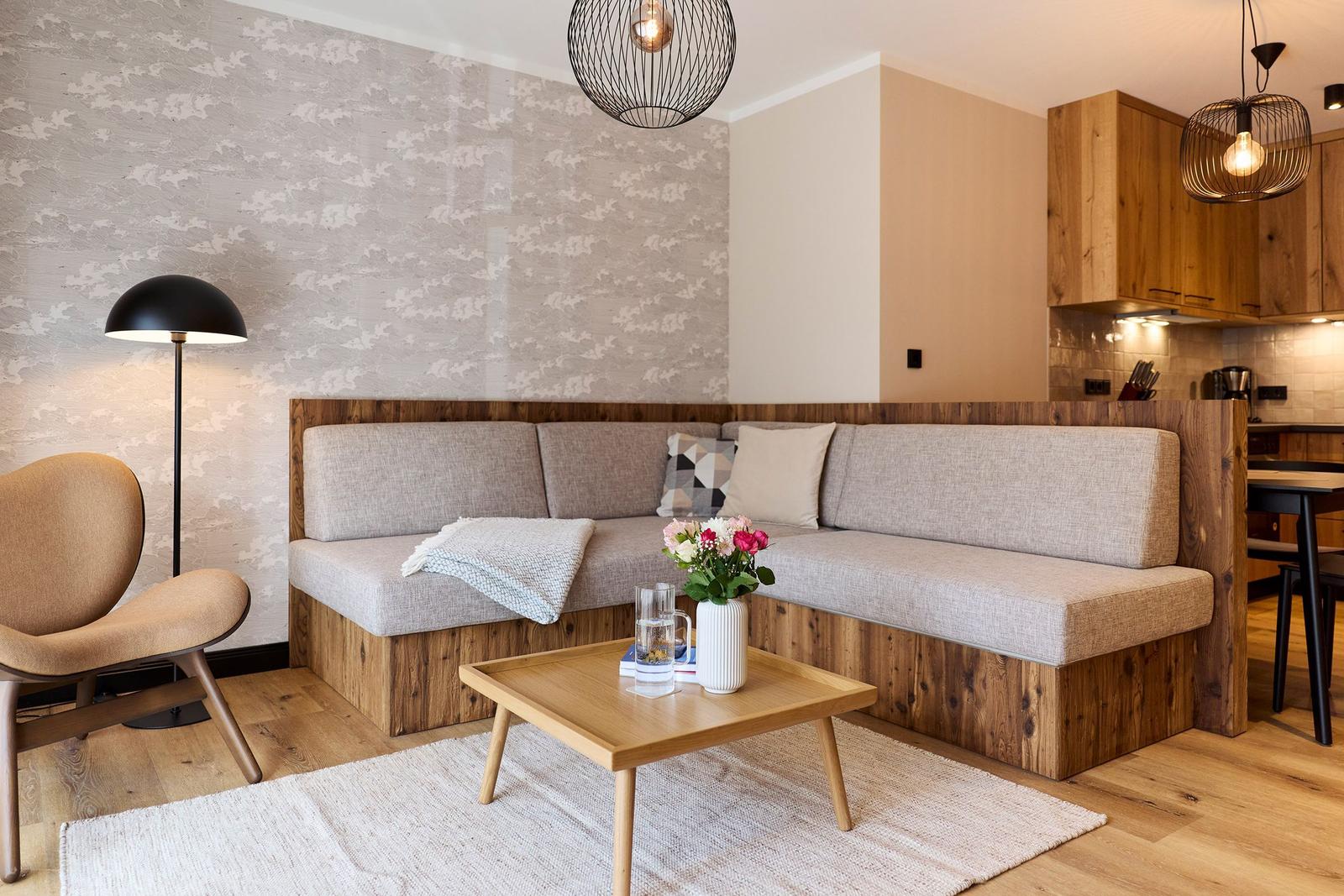 Wohnbereich mit Sofa, Tisch und Stehlampe. Küche im Hintergrund.