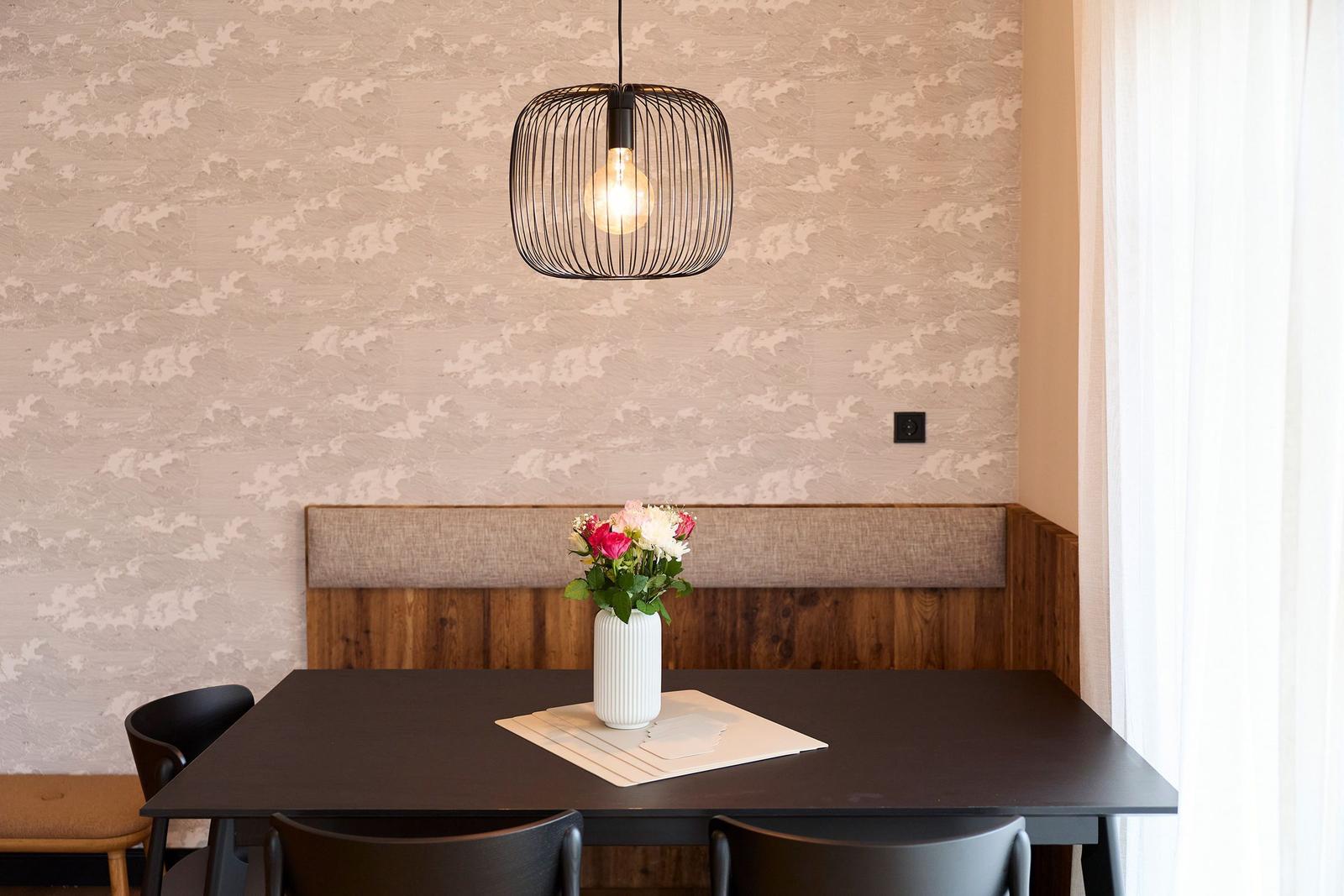 Esstisch mit Stühlen, Blumen und Pendelleuchte vor gemusterter Wand