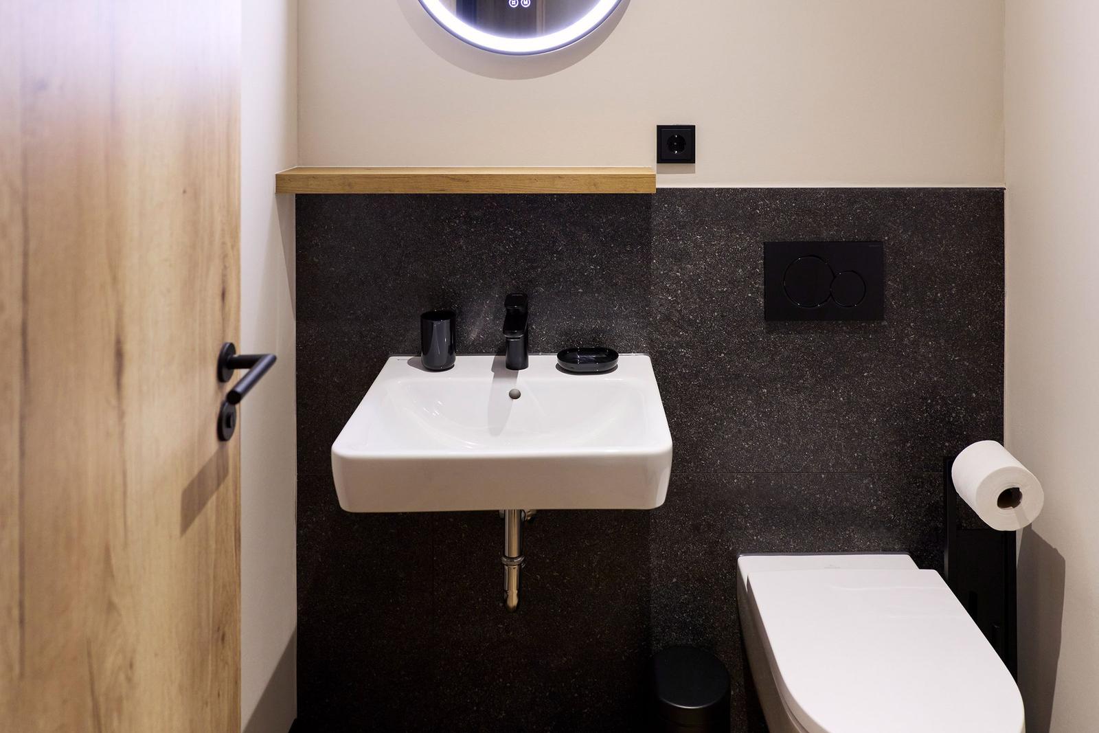Badezimmer mit Waschbecken, Toilette und beleuchtetem Spiegel