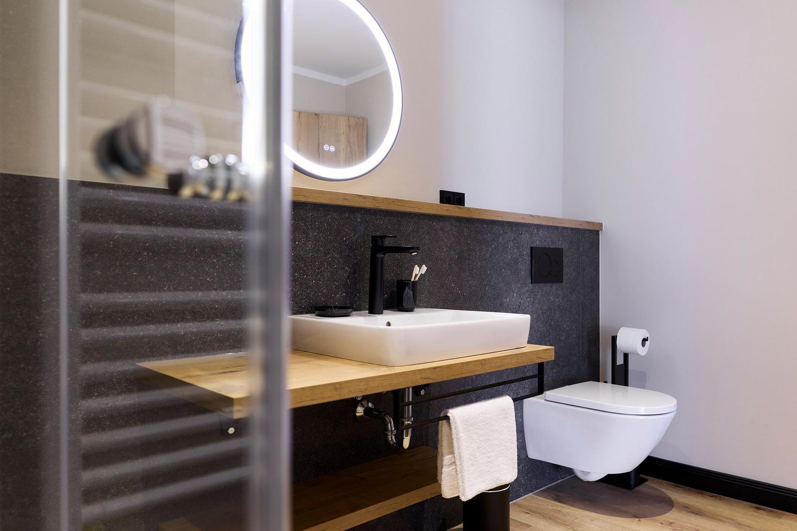 Badezimmer mit Waschbecken, Spiegel und Toilette. Holz- und Steinoptik.
