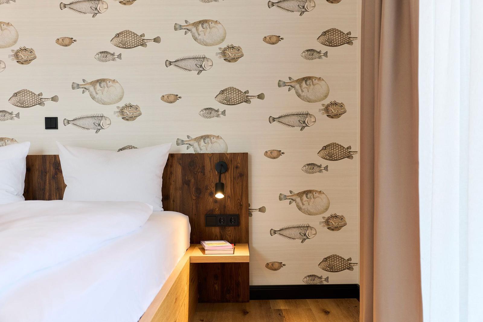 Schlafzimmer mit Fischmotiv-Wandtapete, Holzbett und Nachttisch.