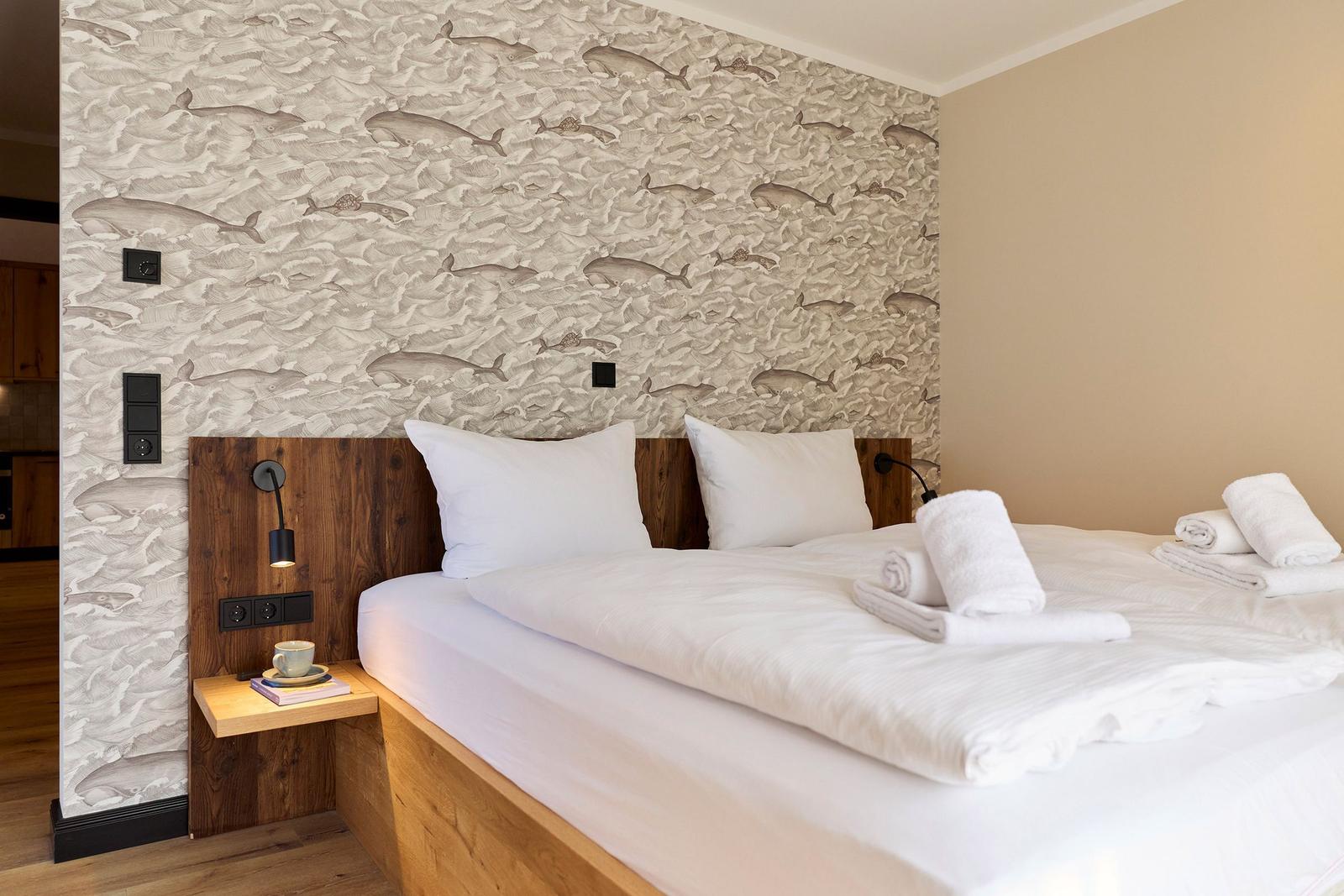 Schlafzimmer mit Bett, Wand mit Walenmotiv und Holzkommode.