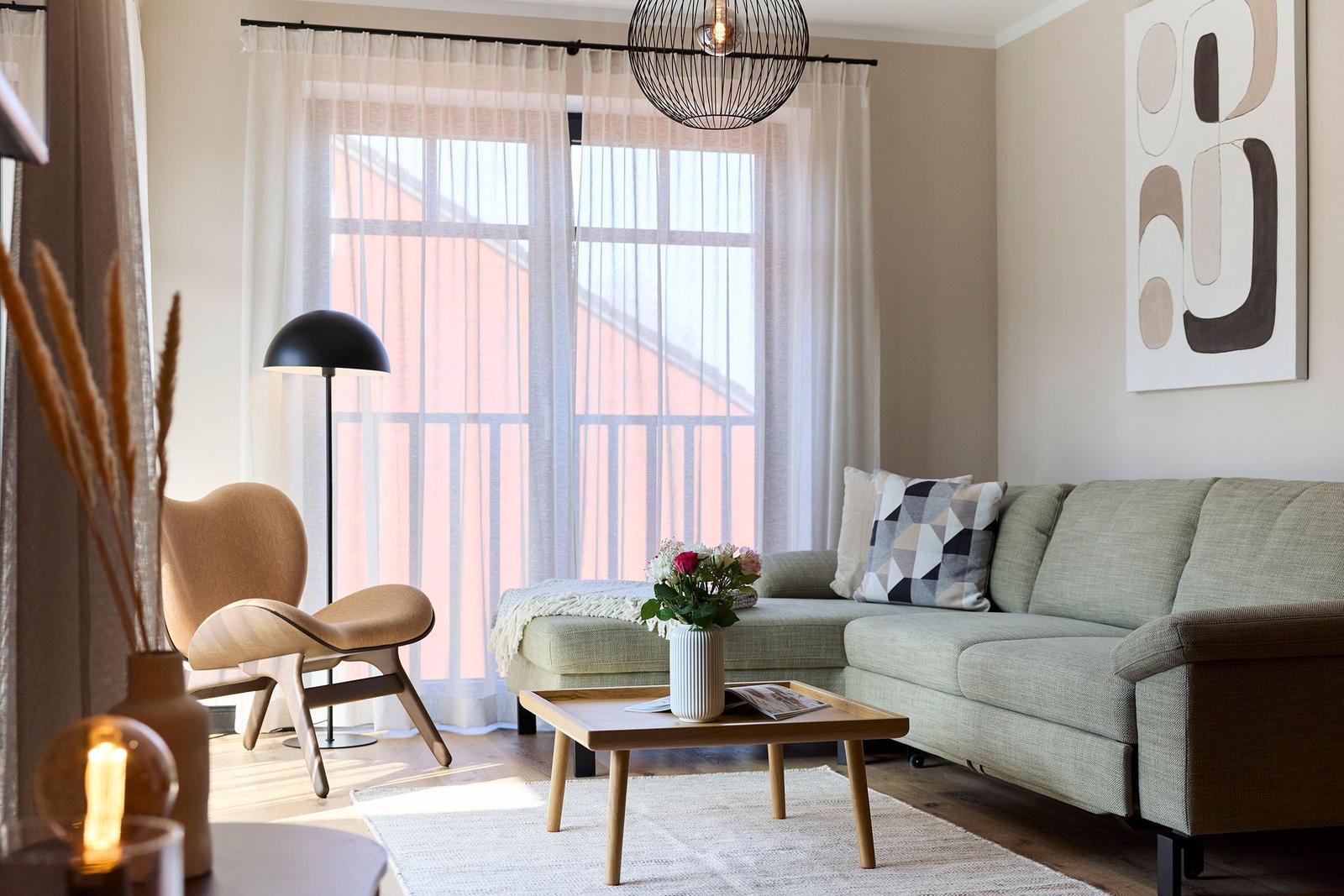 Ein Wohnzimmer mit Sofa, Couchtisch und Sessel vor großem Fenster.