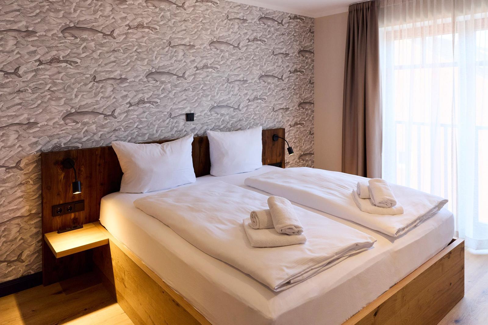 Zimmer mit Doppelbett, Fischmotivwand und Fenster mit Vorhängen.