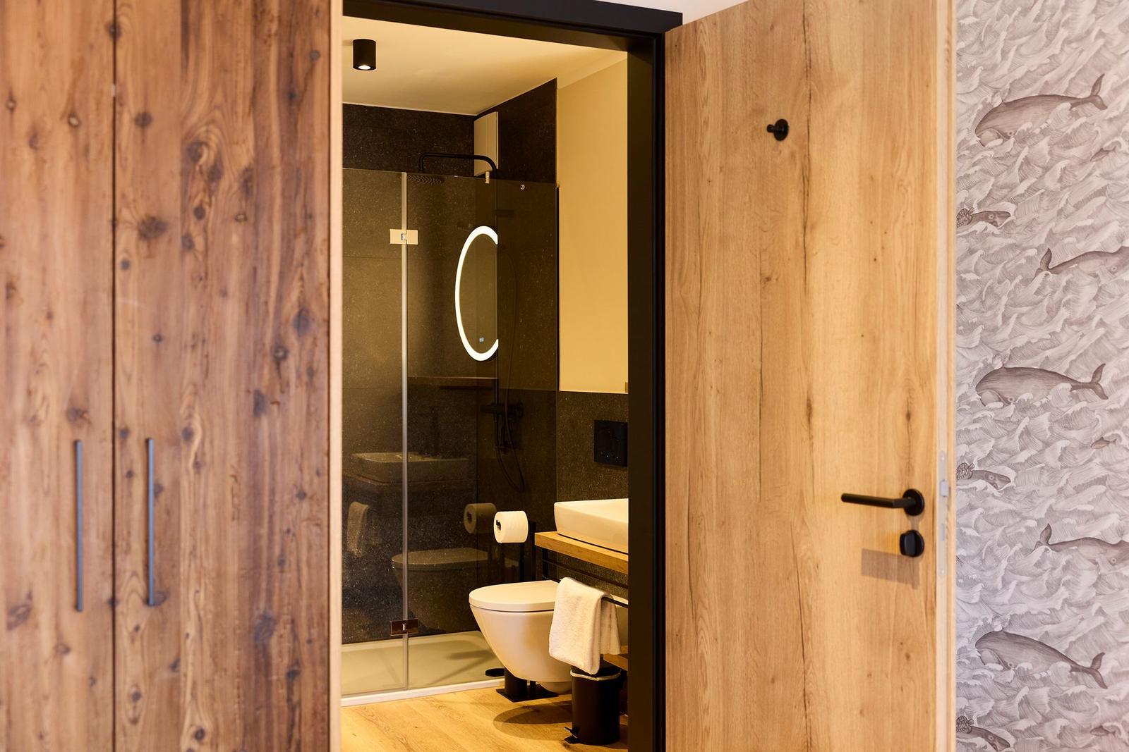 Badezimmer mit Dusche, Toilette und Waschbecken. Holztüren und Wand mit Wal-Motiv.