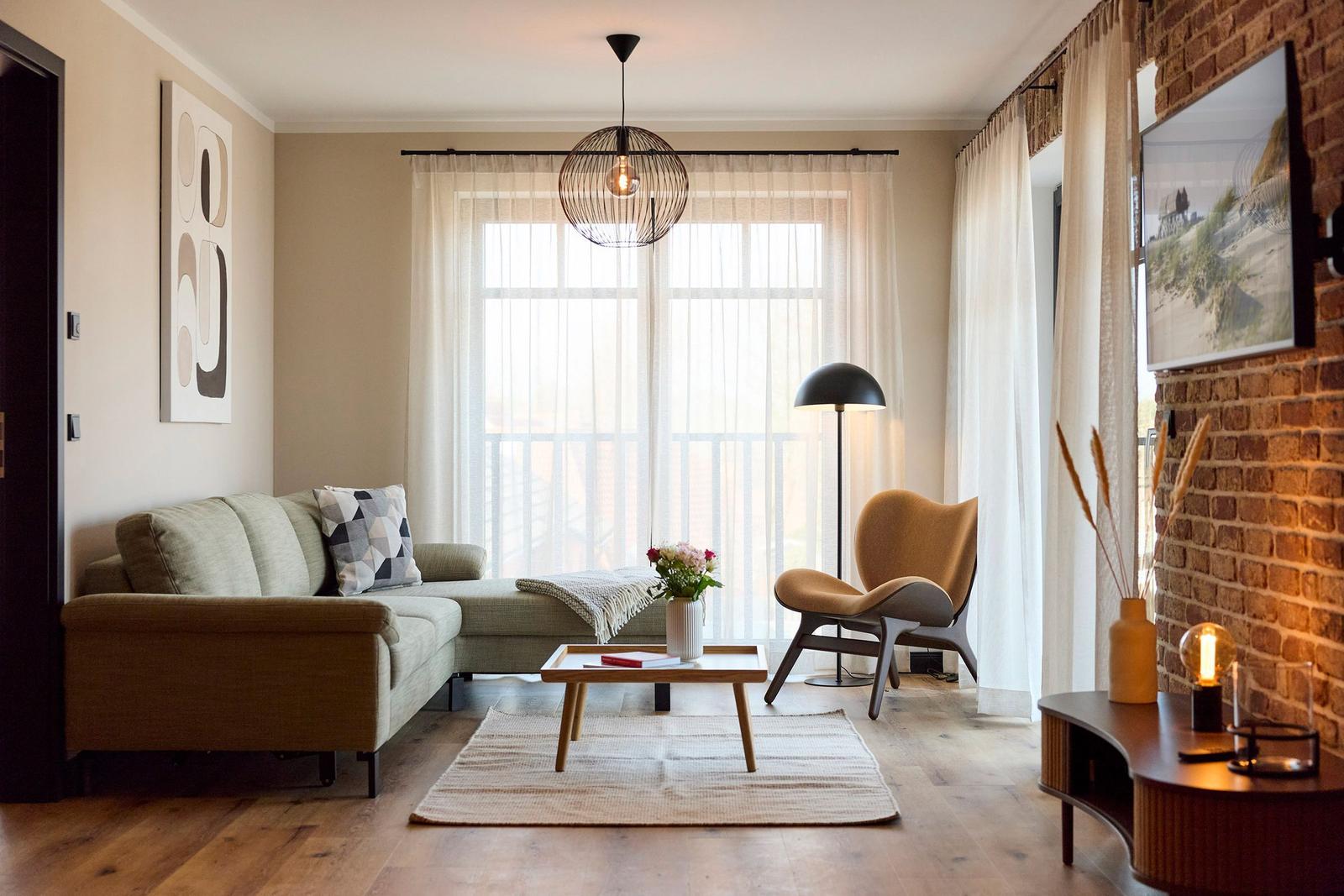 Wohnzimmer mit Sofa, Sessel und Tisch vor Fenster mit Vorhängen.