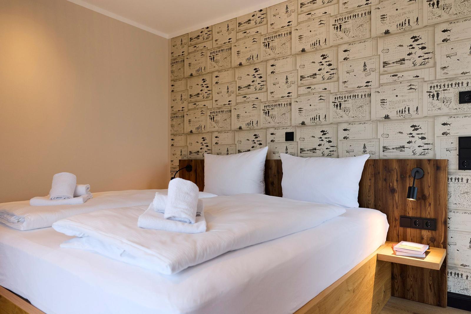Ein Bett mit weißer Bettwäsche und Handtüchern. Wand mit Zeichnungen und Holzkopfteil.