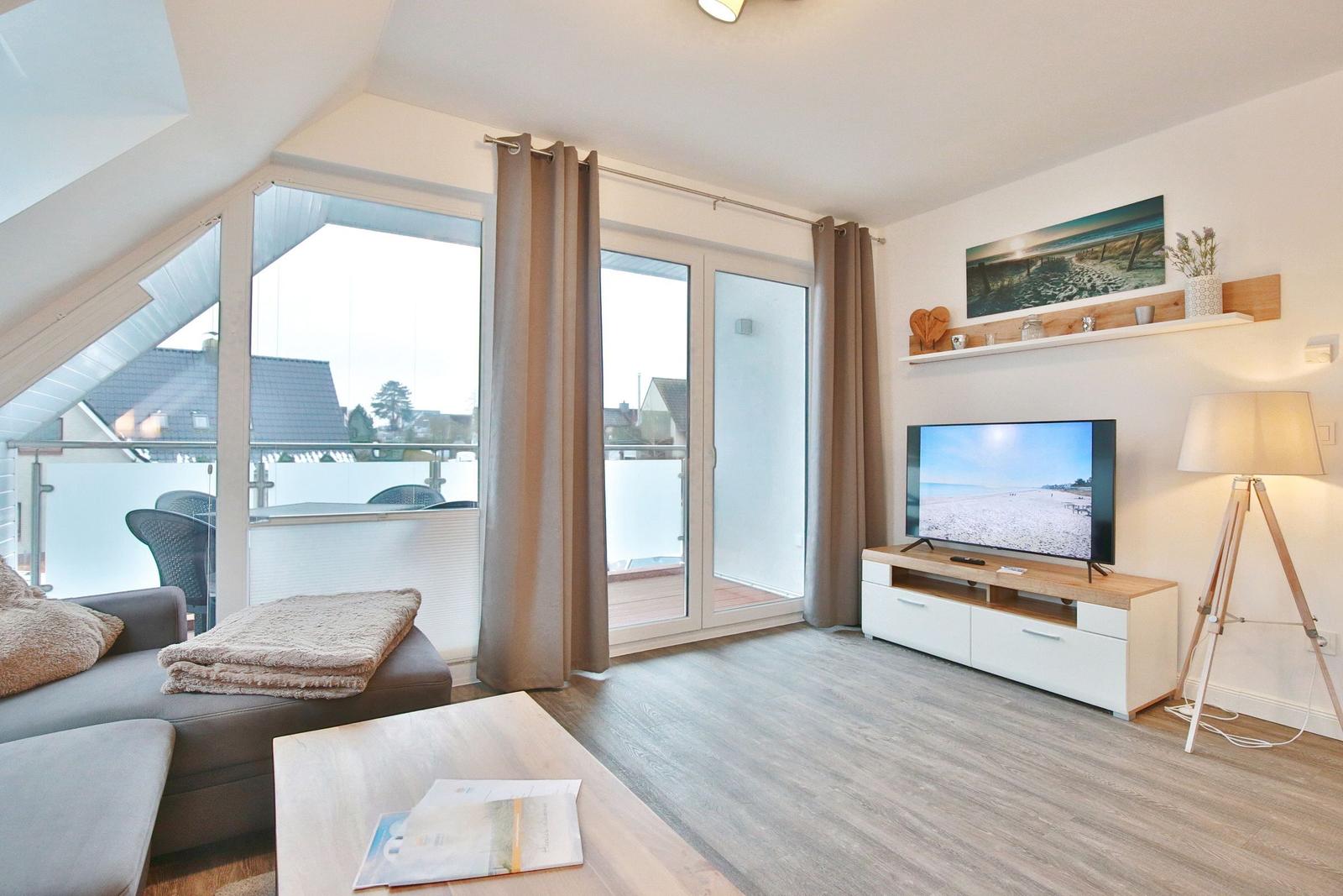 Wohnzimmer mit TV, Balkon und Holzboden. Fenster und Tür führen auf die Terrasse.