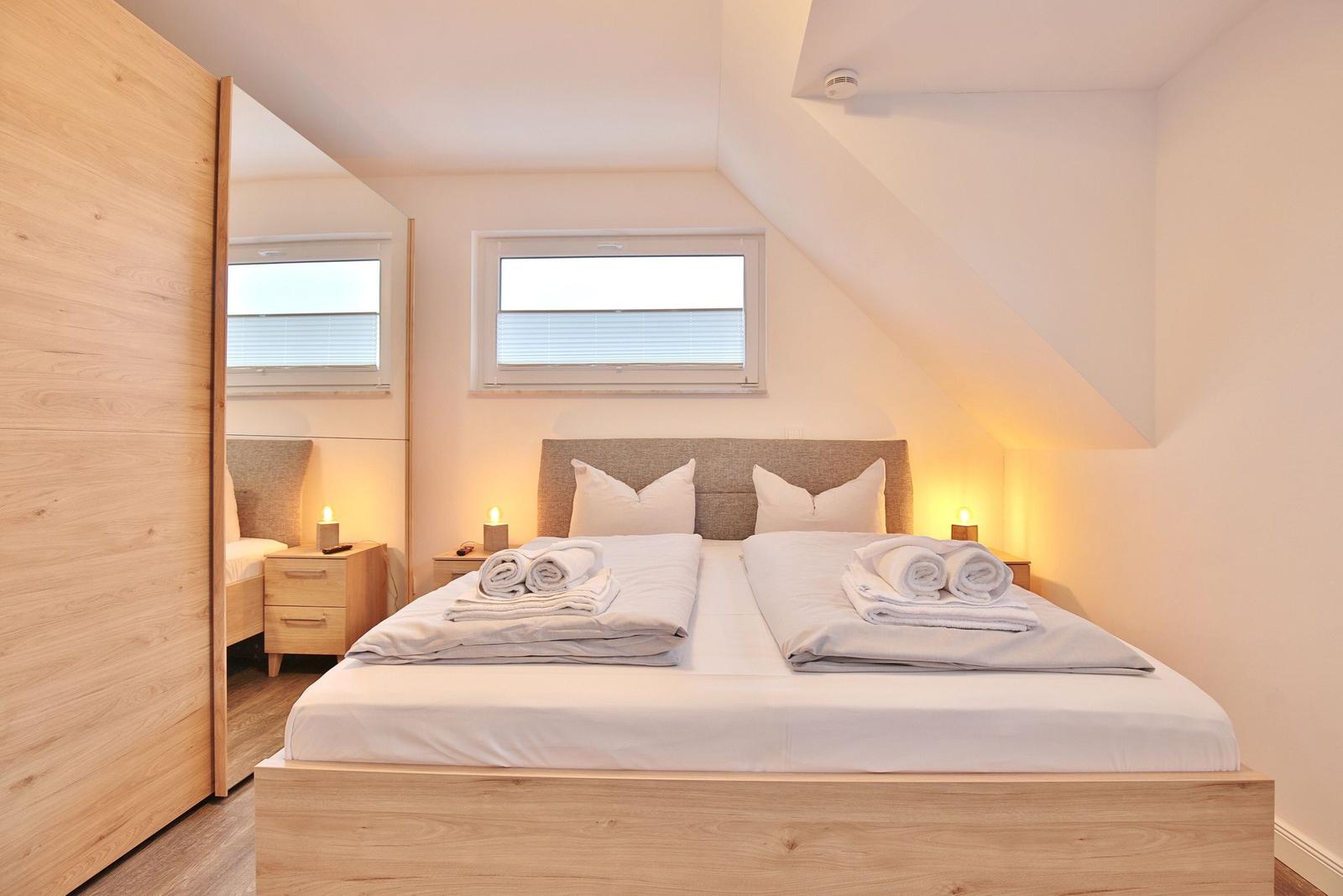 Schlafzimmer mit Doppelbett, zwei Nachttischen und Fenstern unter Dachschrägen.