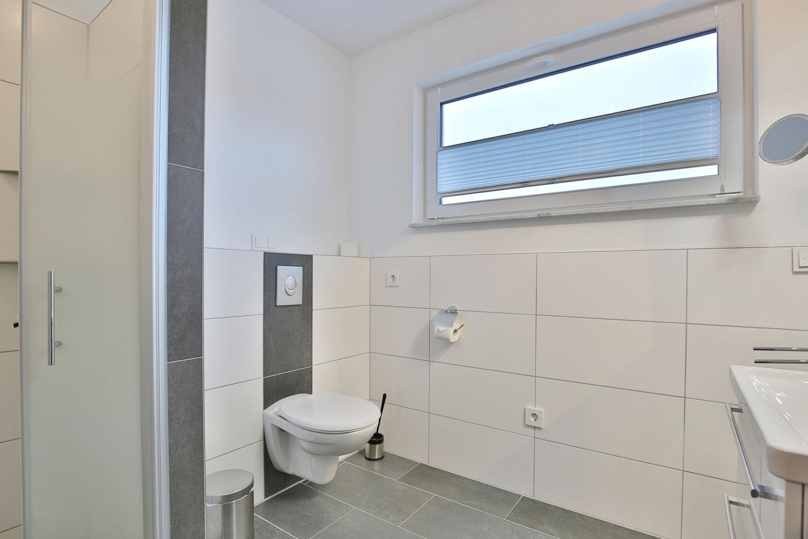 Badezimmer mit Toilette, Waschbecken und Dusche. Fenster mit Jalousie.