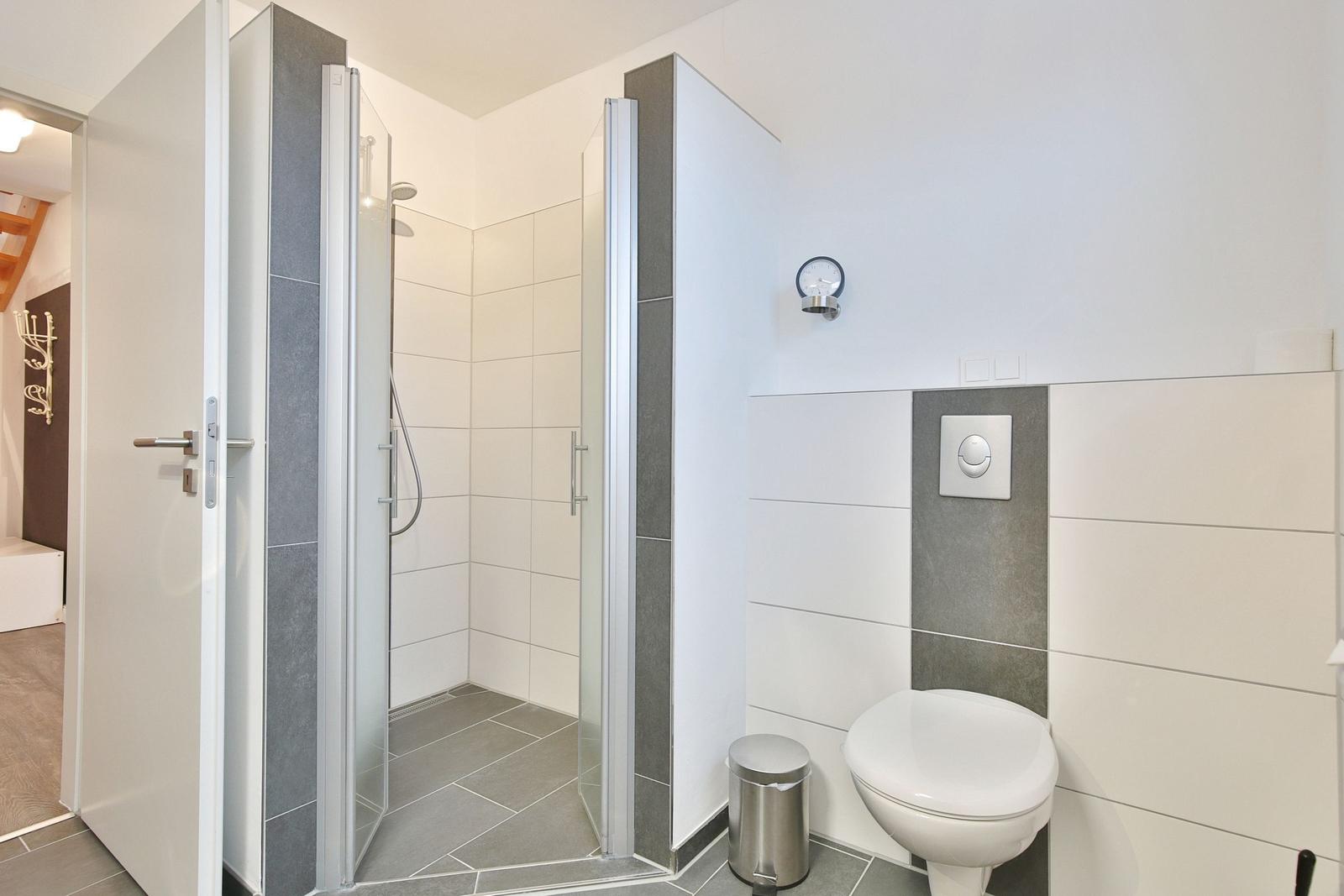 Dusche mit Glaswand, Toilette und integriertem Spiegel an der Wand.