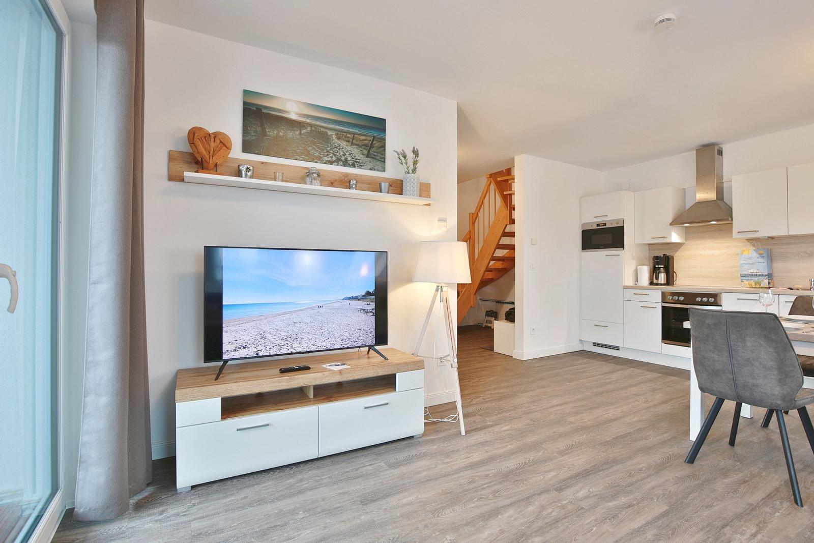 Wohnbereich mit TV, Küchenzeile und Treppe. Holzfußboden und weiße Möbel.