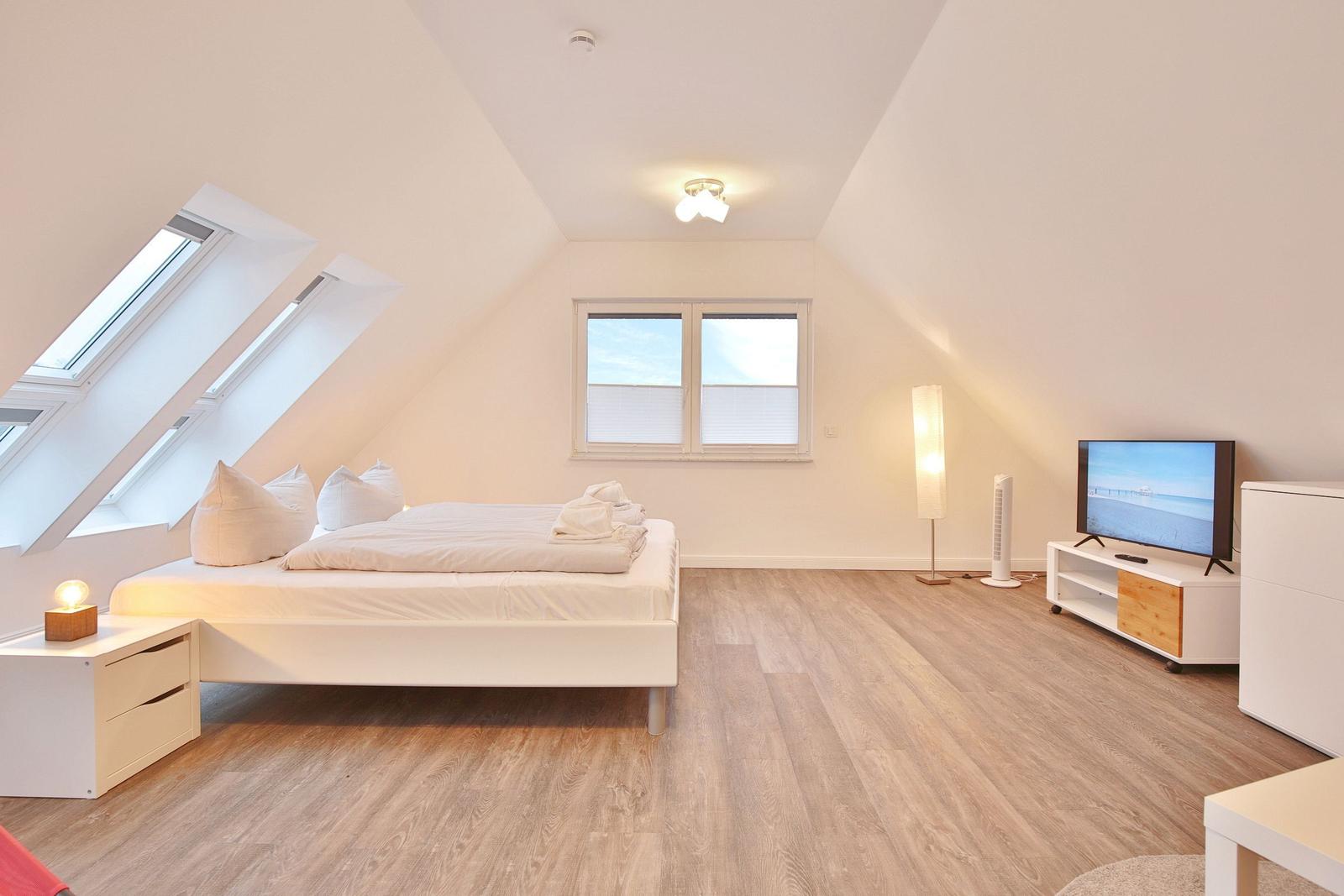 Schlafzimmer mit Dachschrägen, Dachfenstern, Bett, TV und Holzboden.