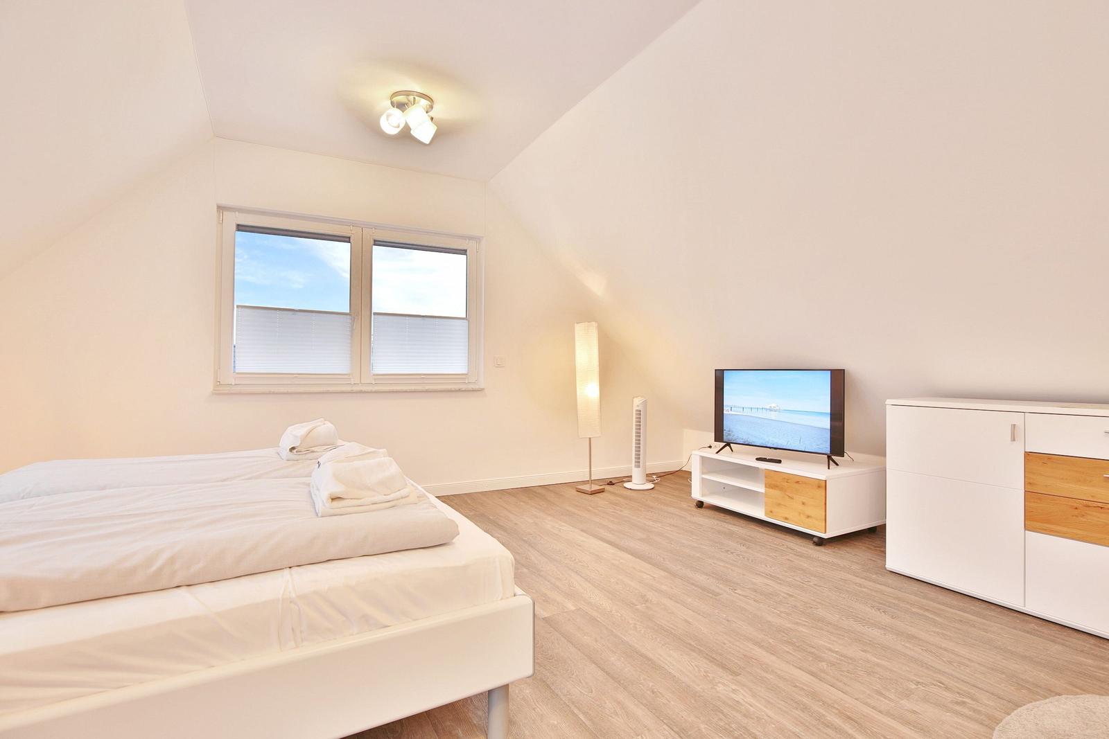 Schlafzimmer mit Bett, TV und Schrank. Holzfußboden und Fenster mit Jalousien.