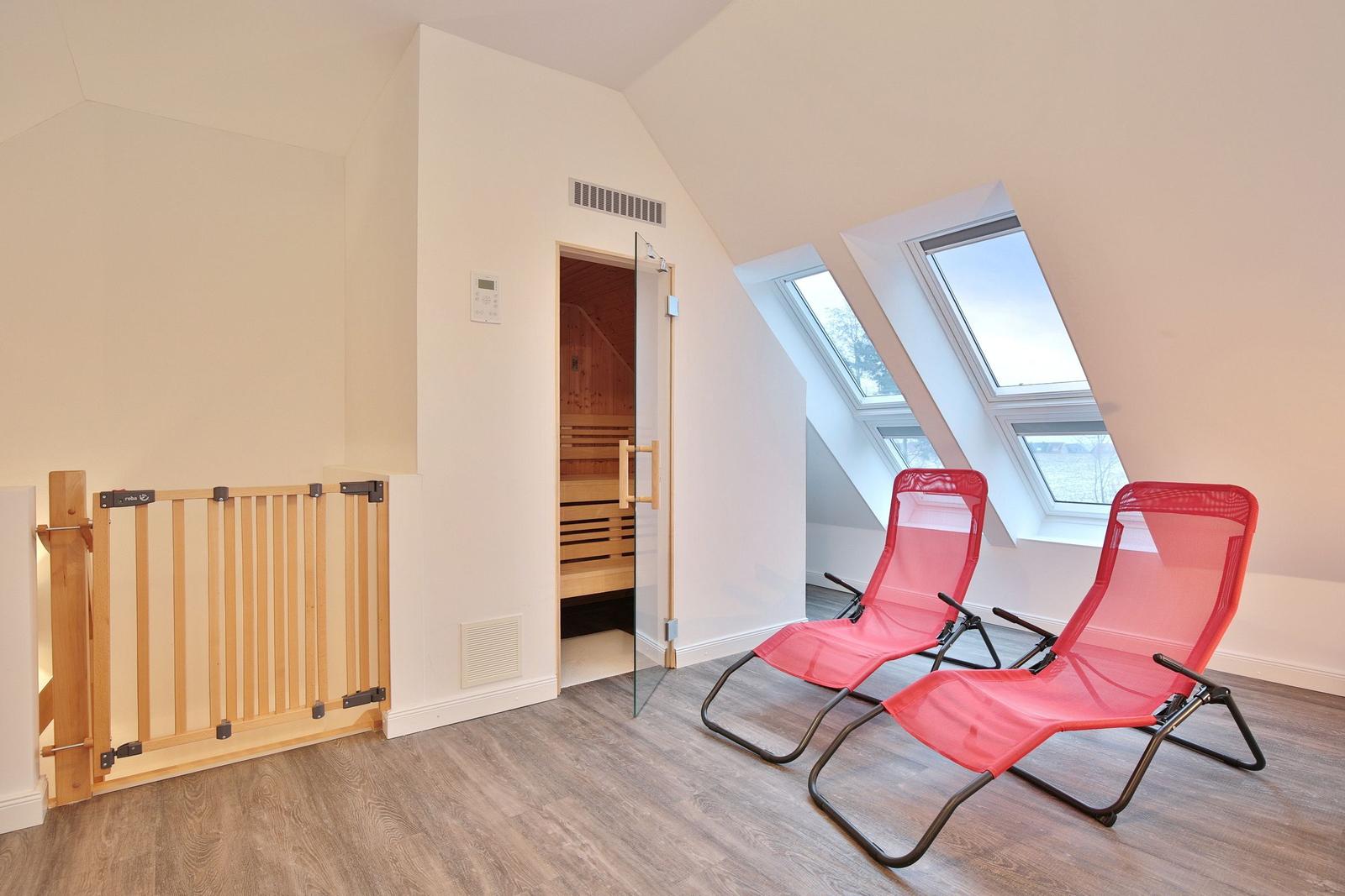 Zwei rote Liegestühle vor Dachfenstern, Sauna mit Glasfront und Kindersicherung.