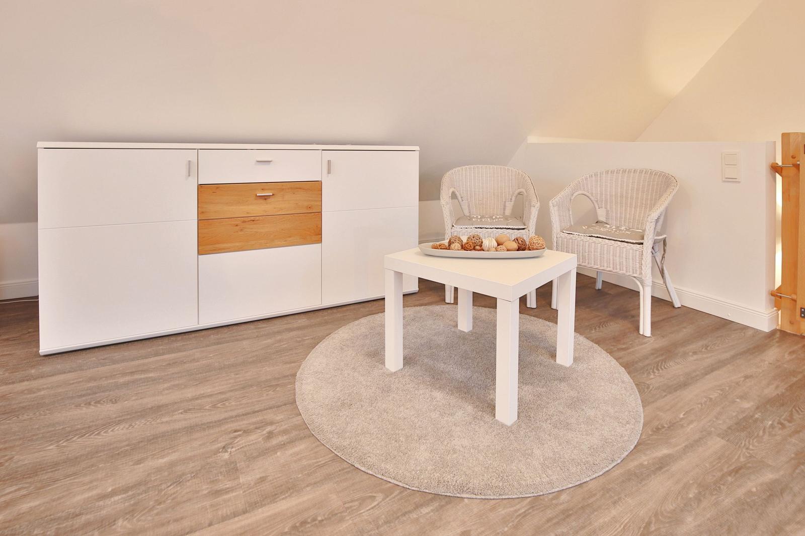 Zimmer mit weißen Stühlen, Tisch und Schrank auf Holzboden.