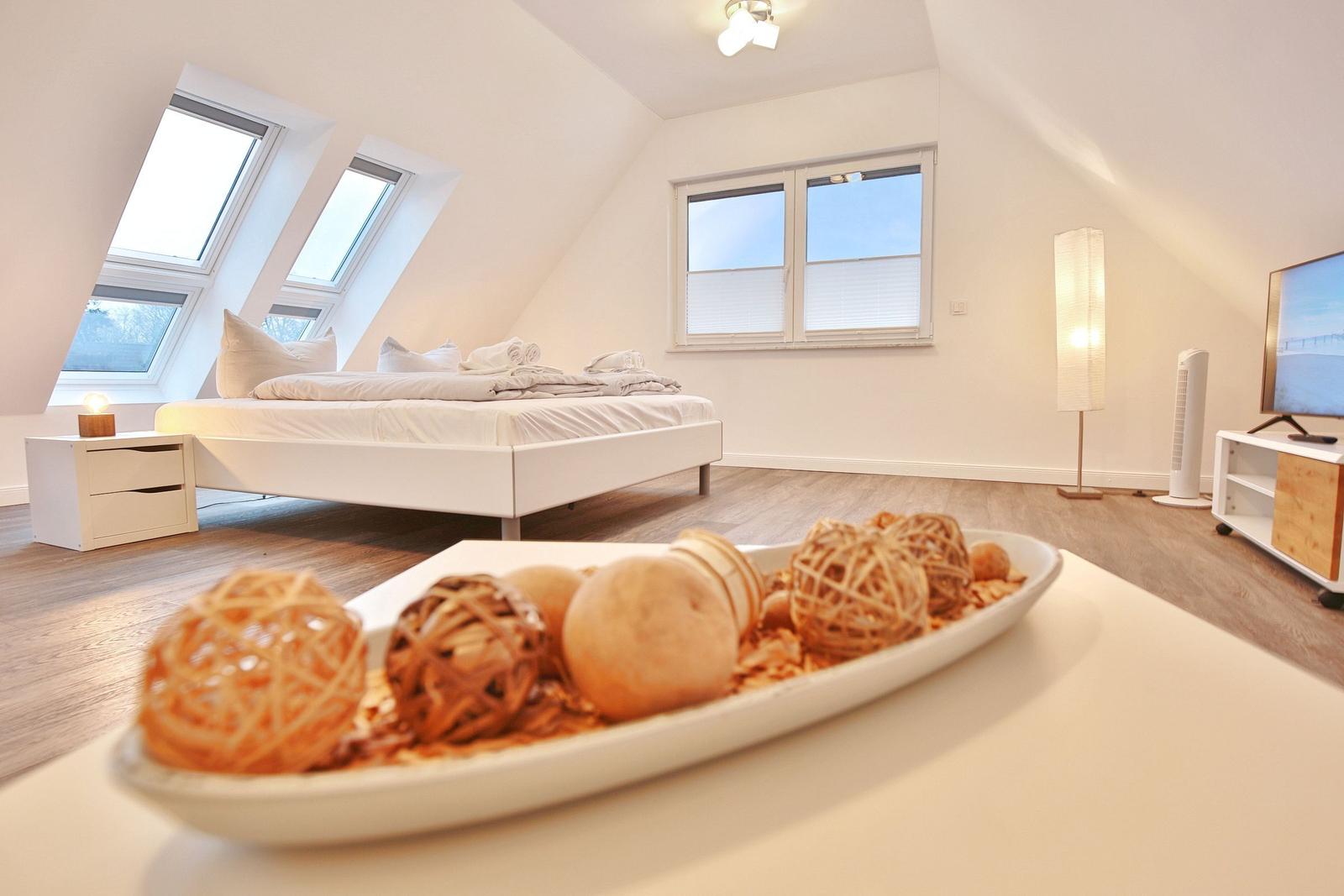 Schlafzimmer mit Dachfenstern, Bett, Fernseher und Tisch mit Dekoration.