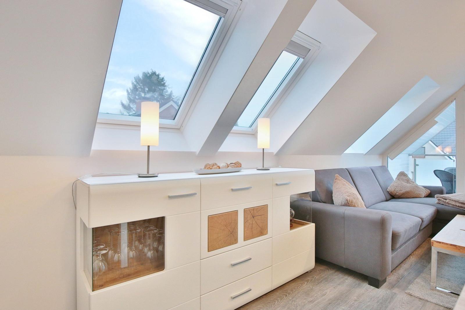 Wohnbereich mit grauem Sofa, weißen Schränken und Dachfenstern.