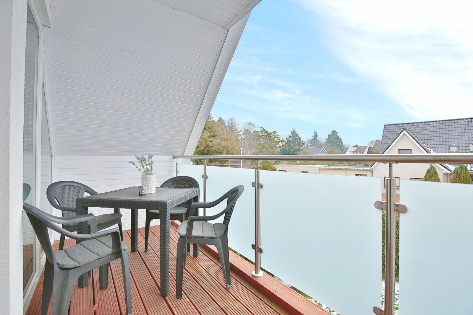 Terrasse mit Tisch und Stühlen, Holzboden und Glasgeländer mit Blick auf Wohngebiet.