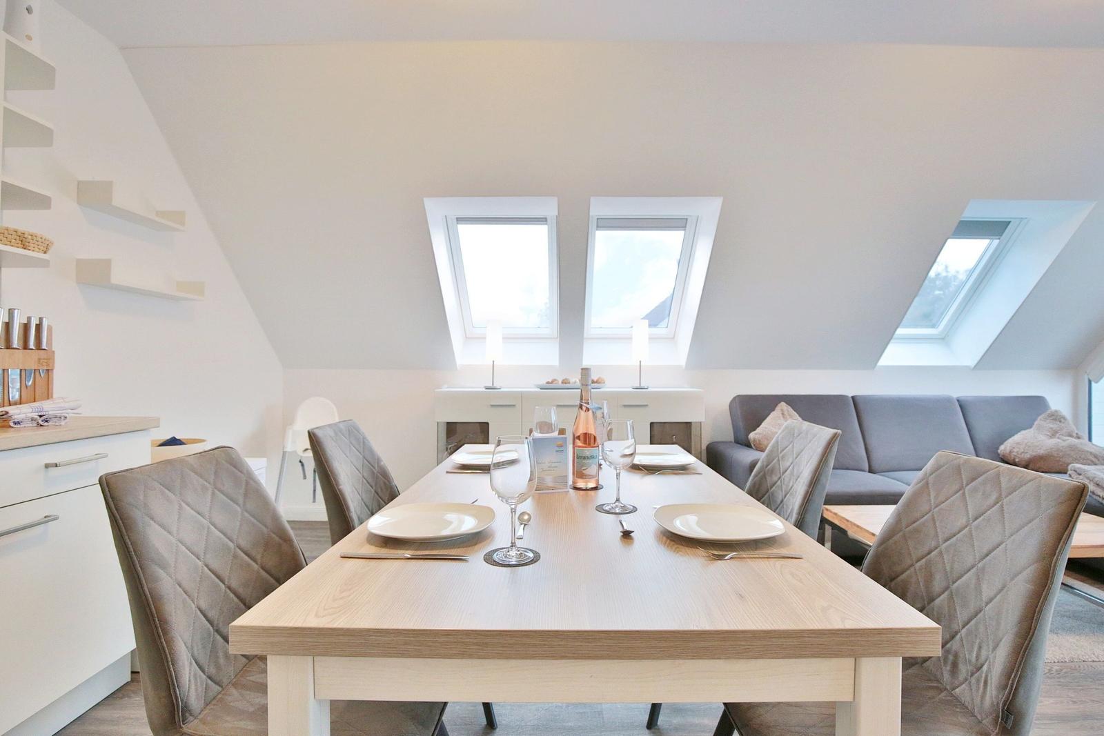 Esszimmer mit Esstisch, Stühlen und Dachfenstern. Küche und Sofa im Hintergrund.
