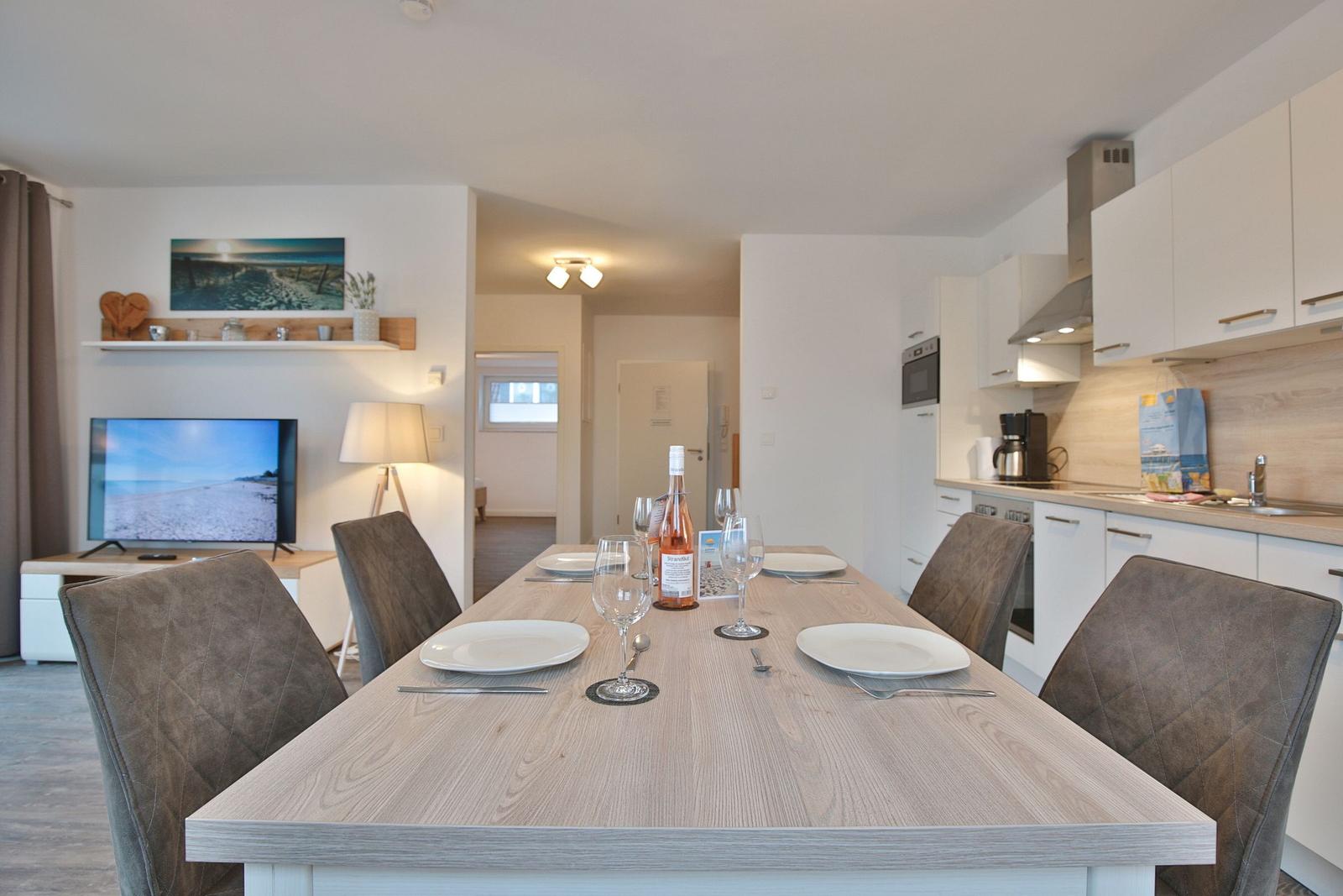 Essbereich mit Tisch und Stühlen, Küche und Wohnzimmer im Hintergrund.