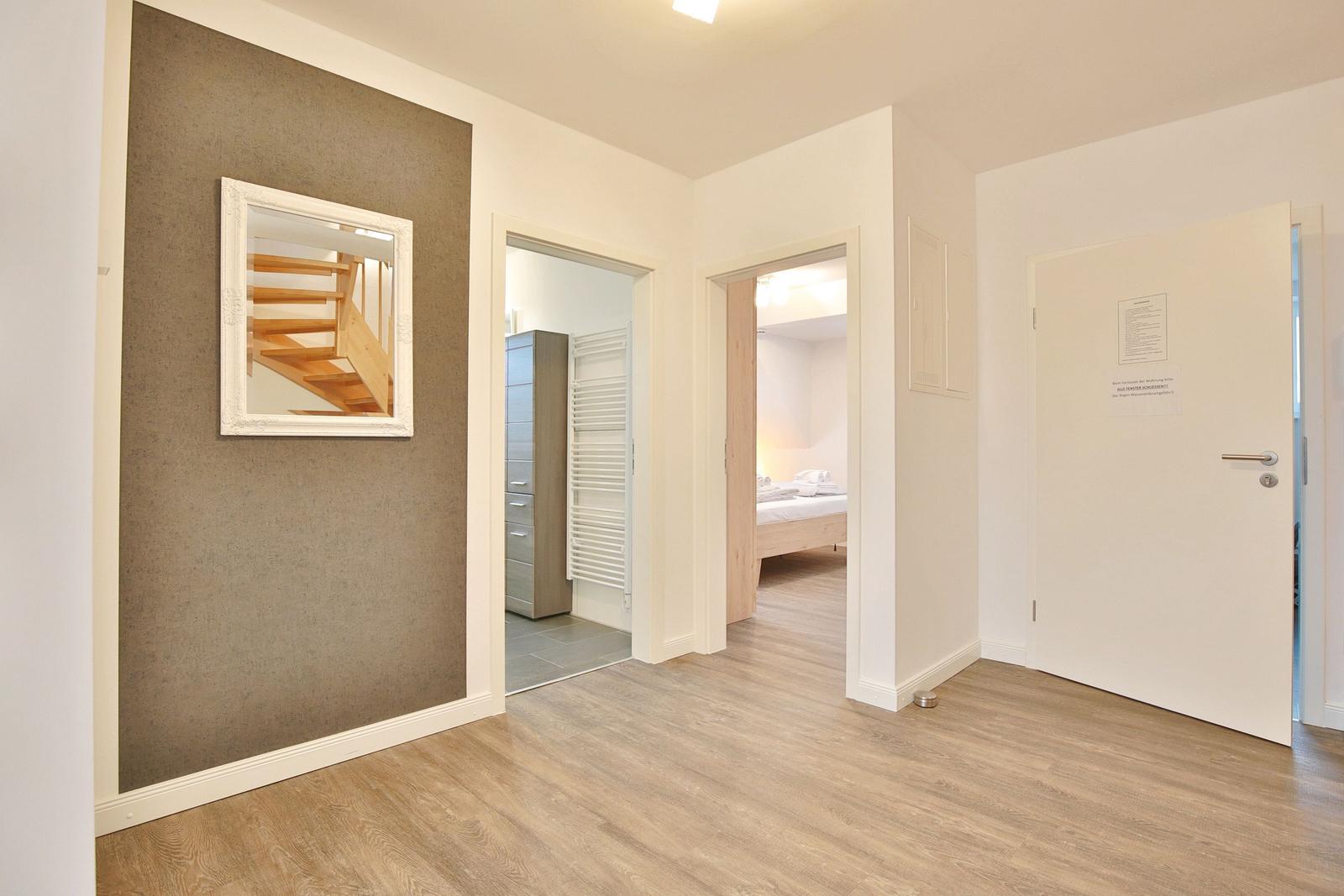 Flur mit Holzboden, Spiegel an der Wand und Blick in Schlafzimmer und Bad.