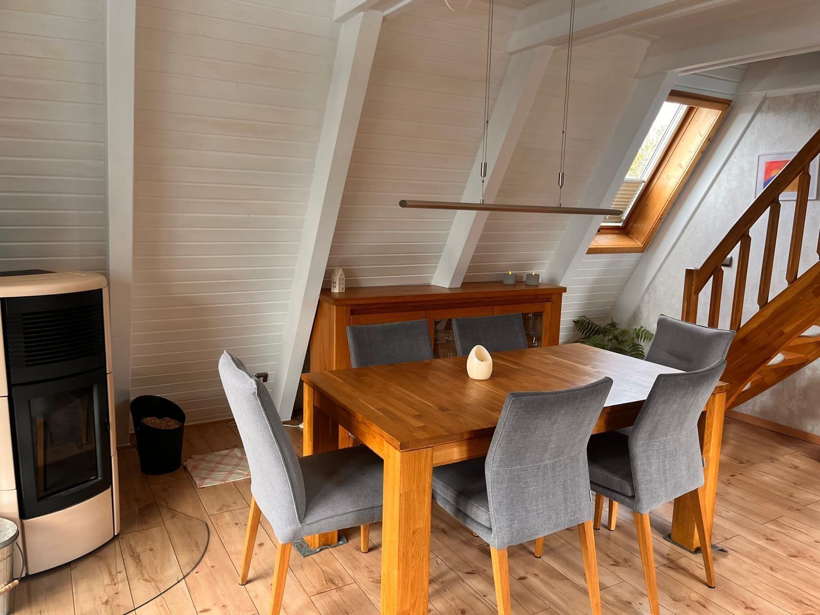 Essbereich mit Holztisch, grauen Stühlen und Dachfenster. Holzfußboden und weiß verkleidete Wände.